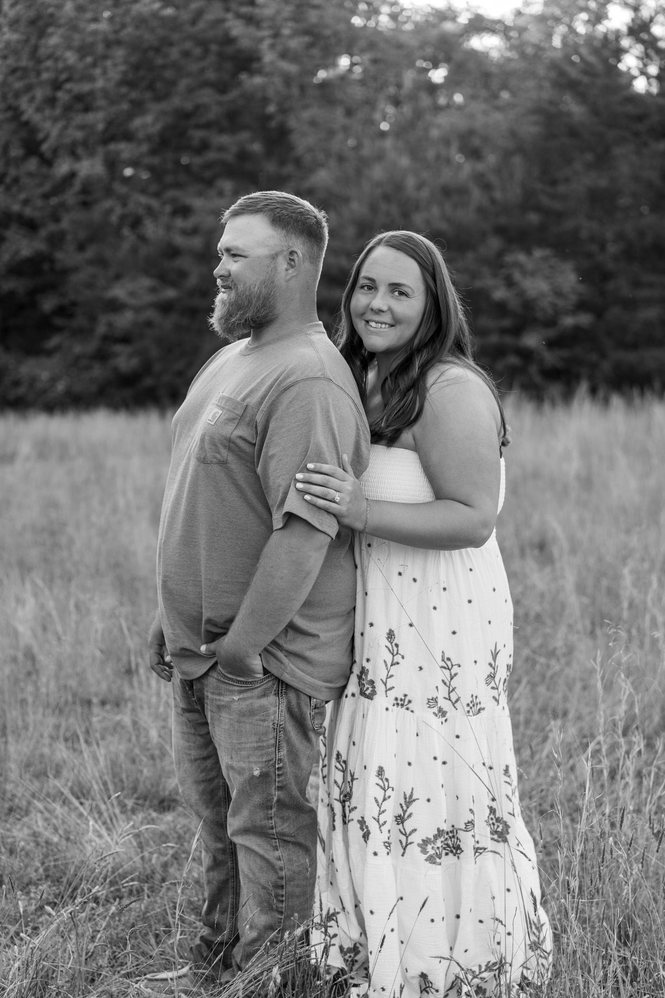 Black and white portrait of engaged couple embracing in open field.