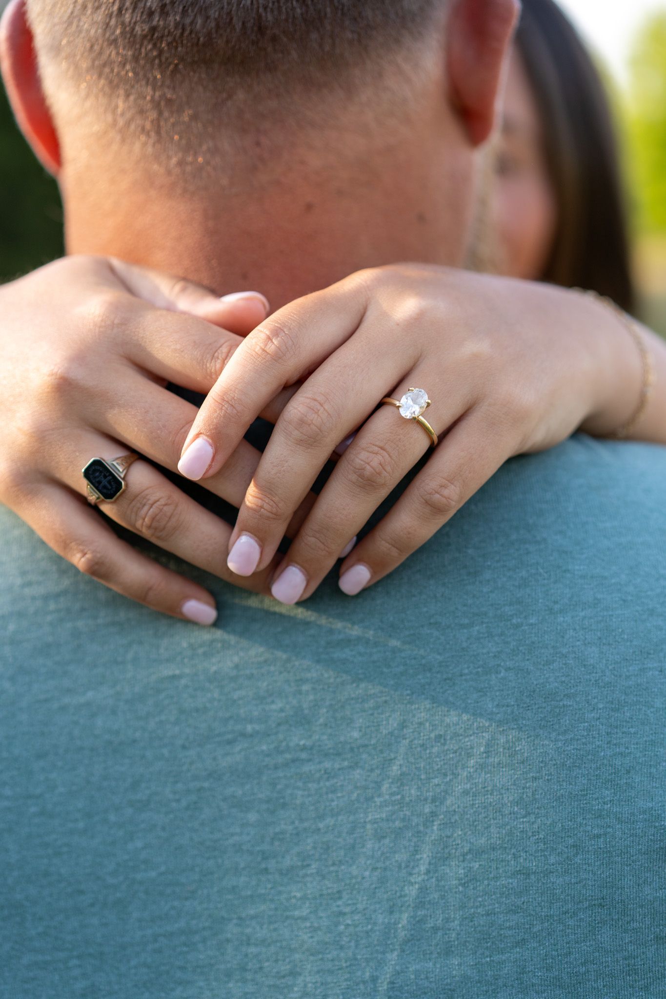 Close-up of couple embracing showing diamond engagement ring and black band on woman's hand.