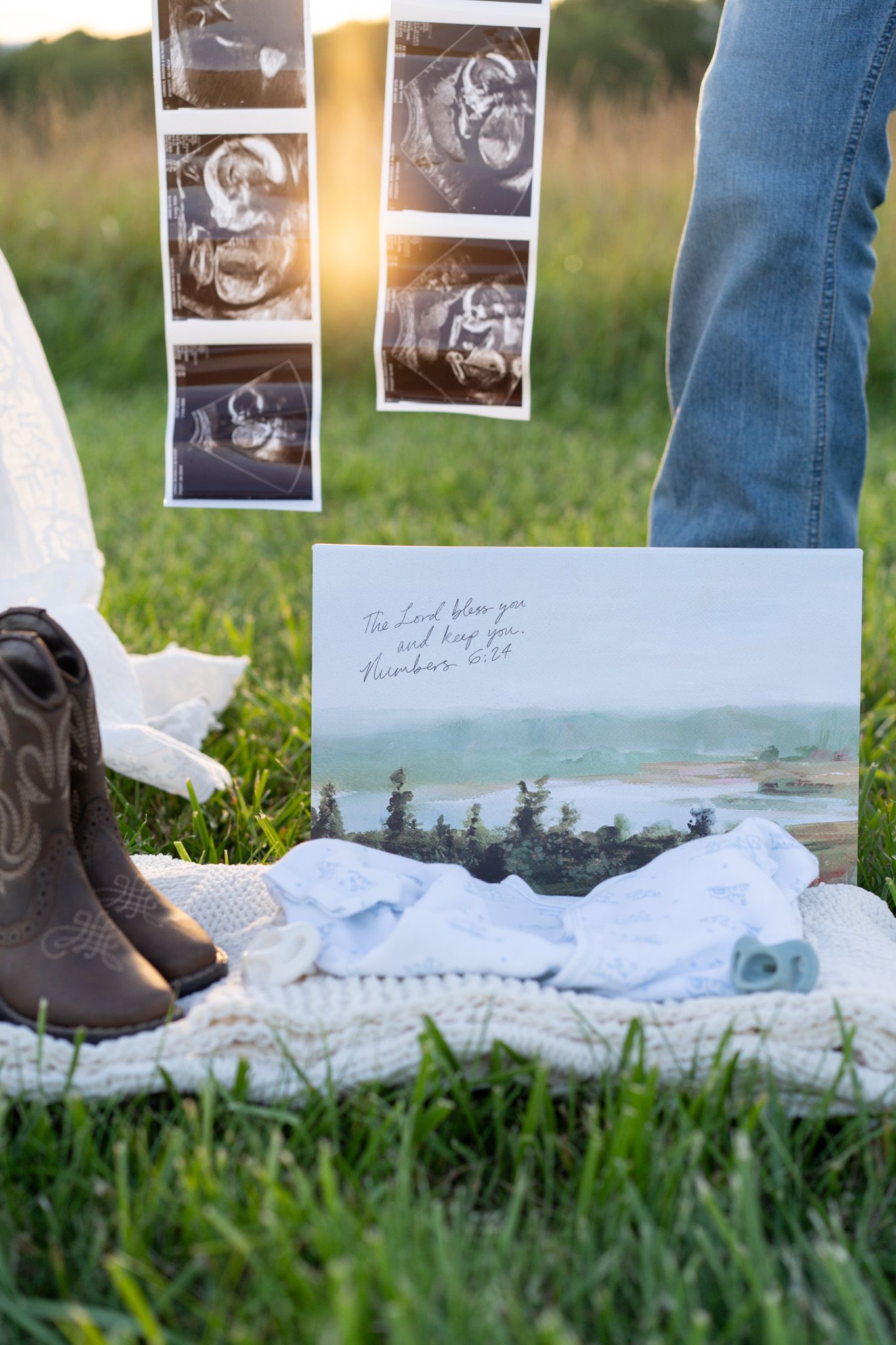 Maternity flat lay with ultrasound photos, baby shoes, white onesie, and a scenic landscape print card.