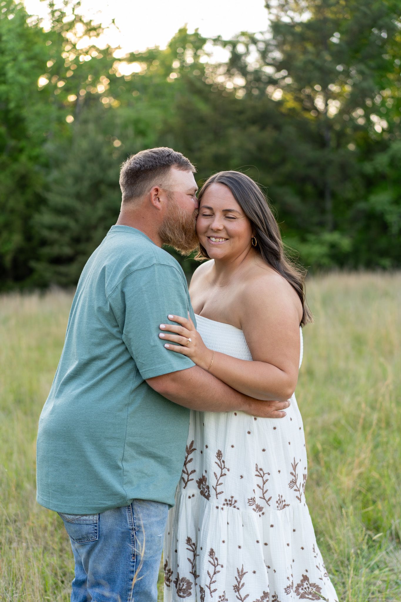 Happy couple embracing and laughing in a lush green meadow at sunset.