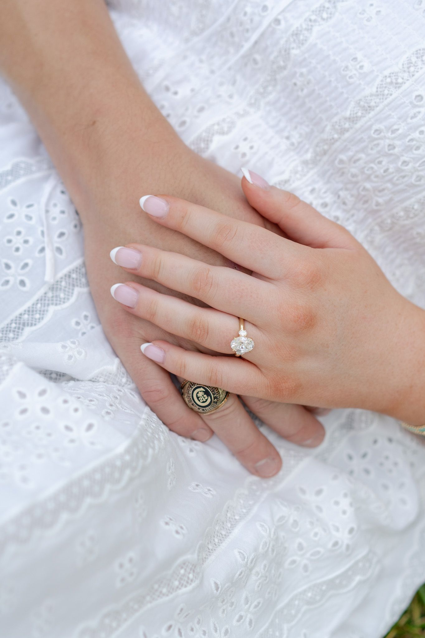 Close-up of woman's hands showing a diamond engagement ring on white eyelet lace dress fabric.