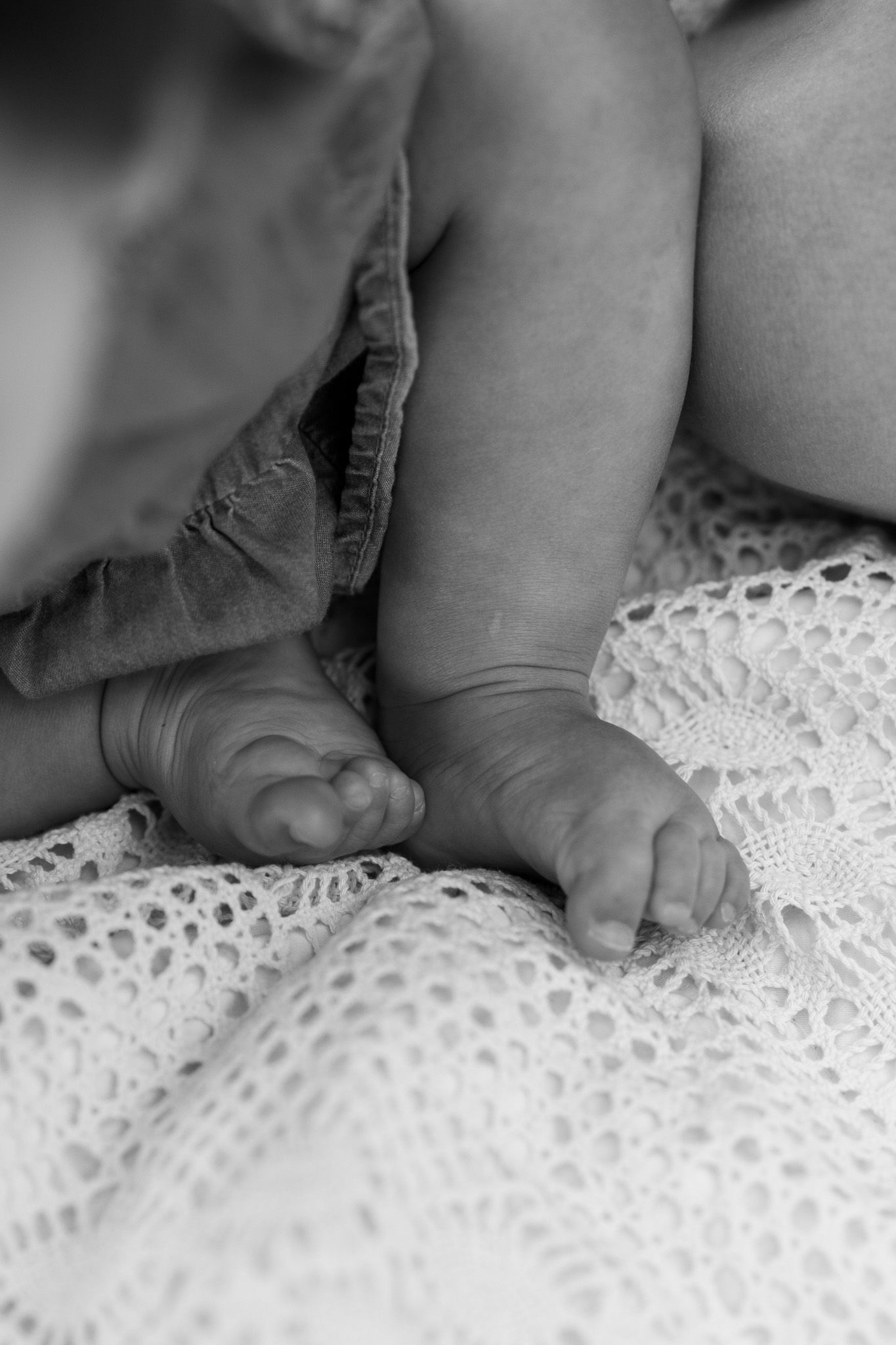 Black and white close-up of tiny baby feet resting on textured white crochet blanket outdoors.