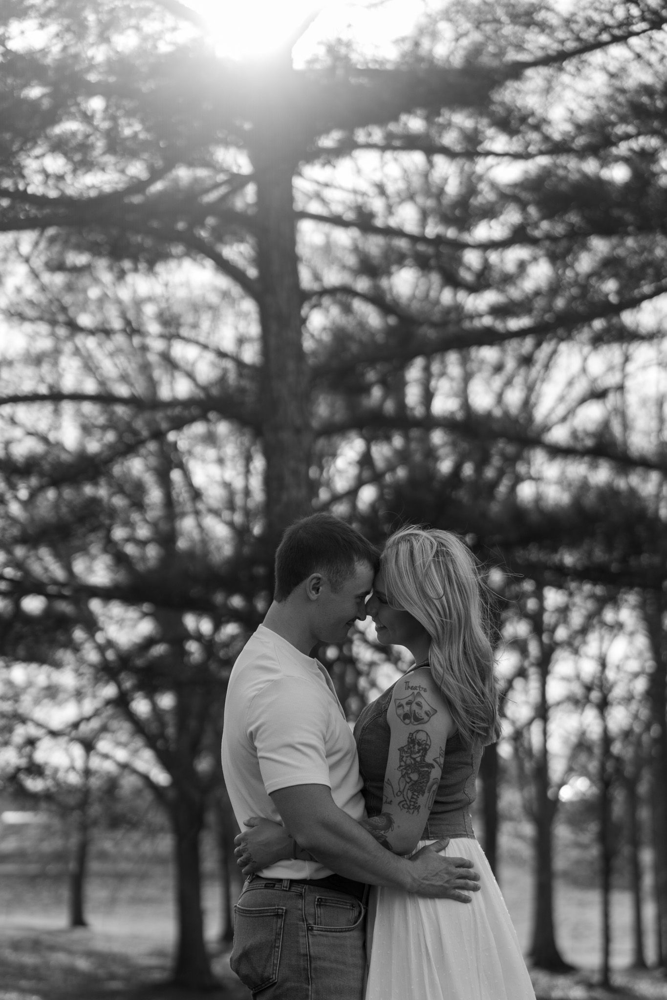 Black and white romantic couple touching foreheads under sunlit trees in a park.