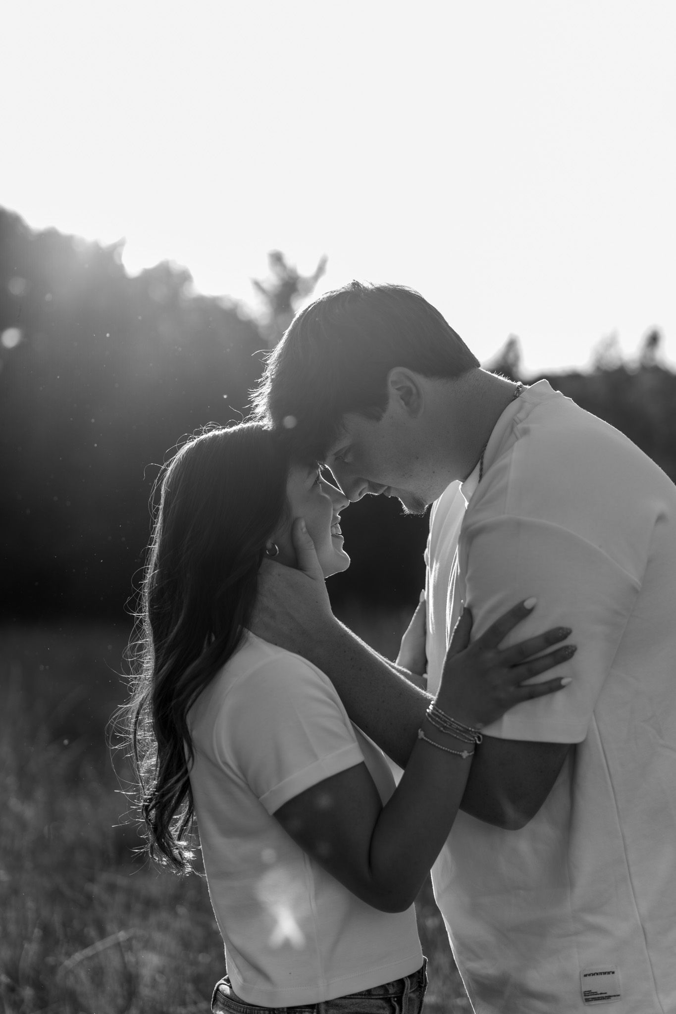 Black and white romantic couple embracing and laughing together in a bright sunlit field.