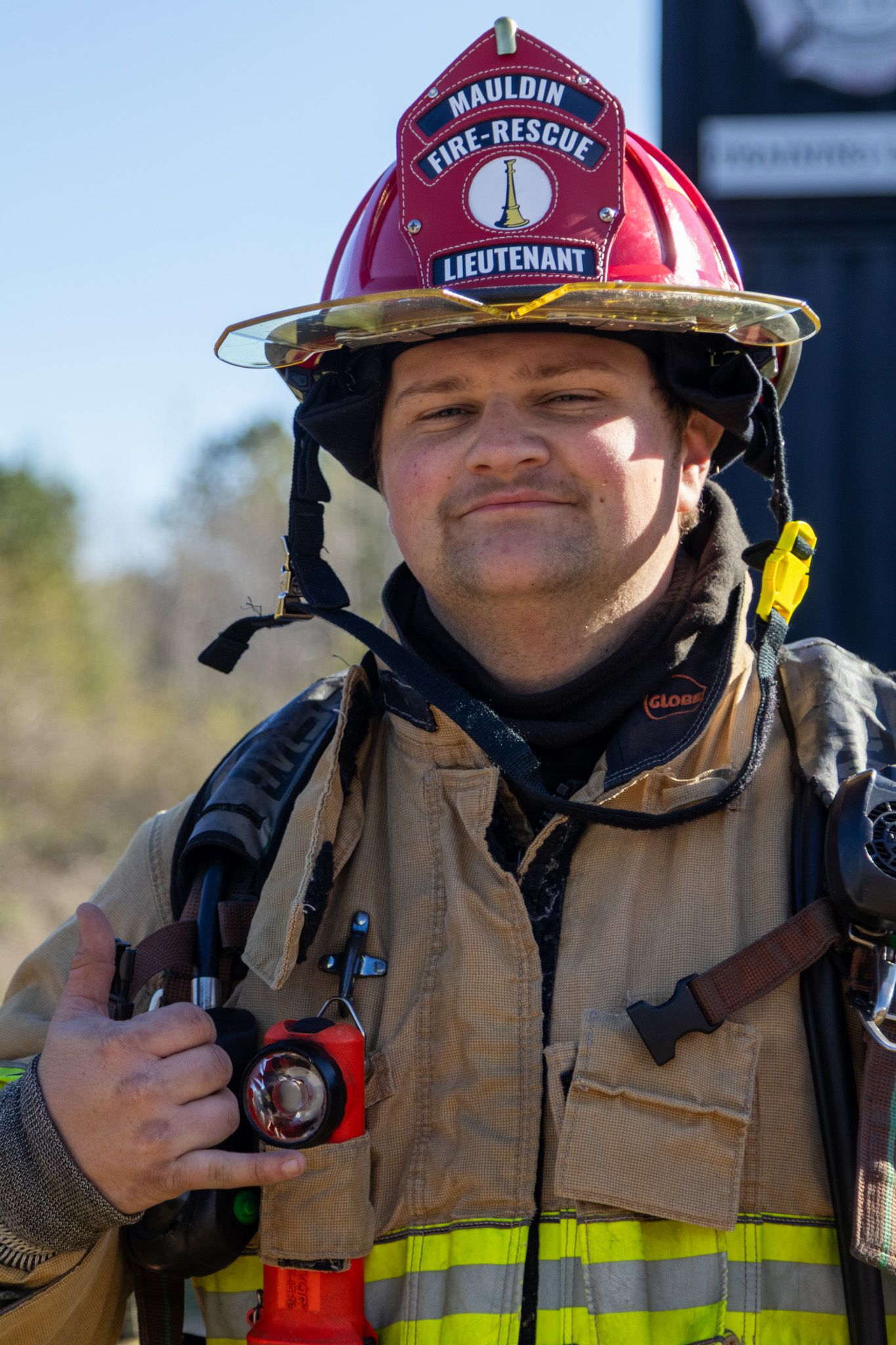 Mauldin Fire-Rescue Lieutenant in red helmet and turnout gear holding a radio outdoors.