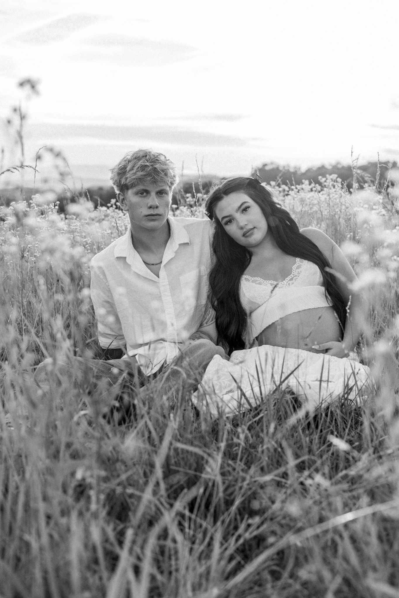 Black and white photo of a young couple sitting together in a wildflower field at dusk.