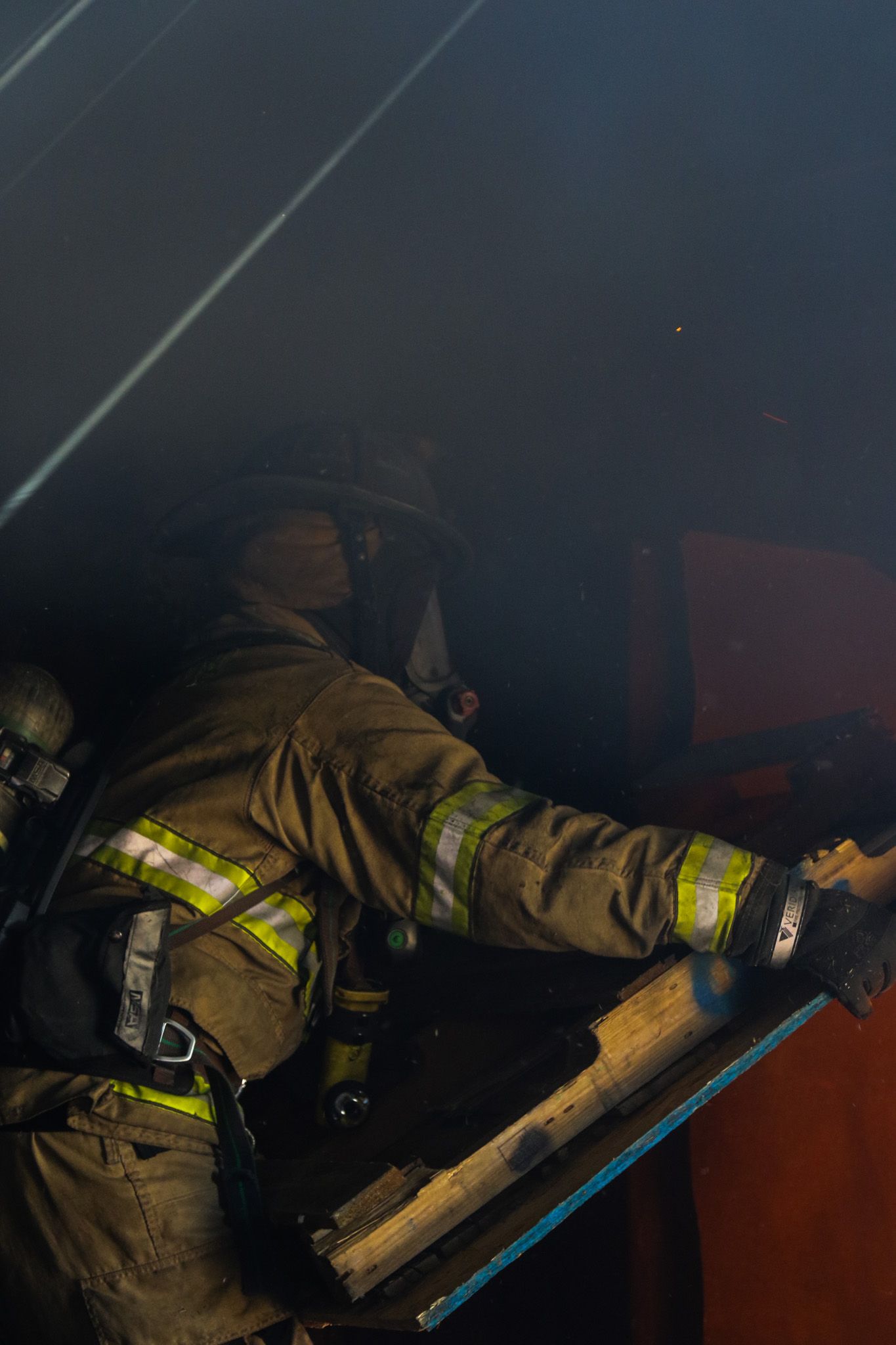 Firefighter in full protective gear with reflective stripes works through smoke during an active fire rescue operation.