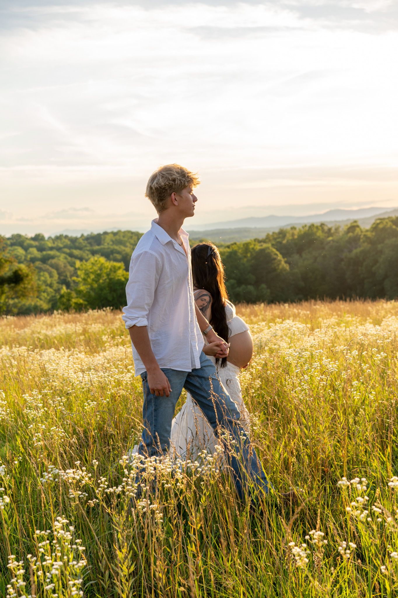 Couple walking in golden wildflower field at sunset with mountain views behind them.