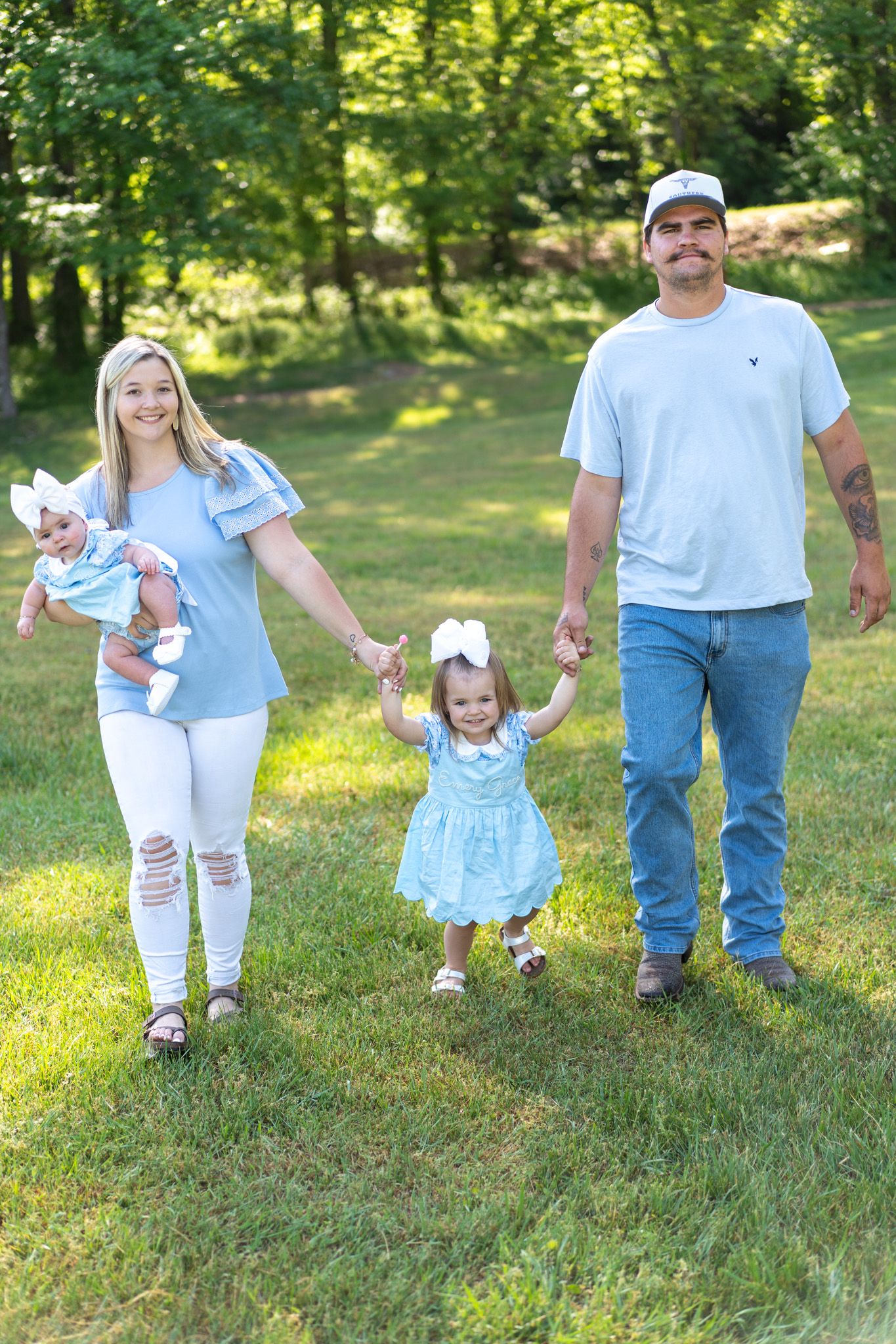 Joyful family of four walking hand-in-hand through a lush green park on a sunny day.