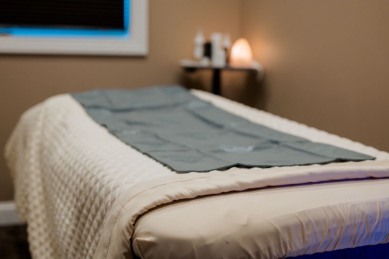 Spa massage table with gray blanket in a softly lit treatment room with warm ambient lighting.