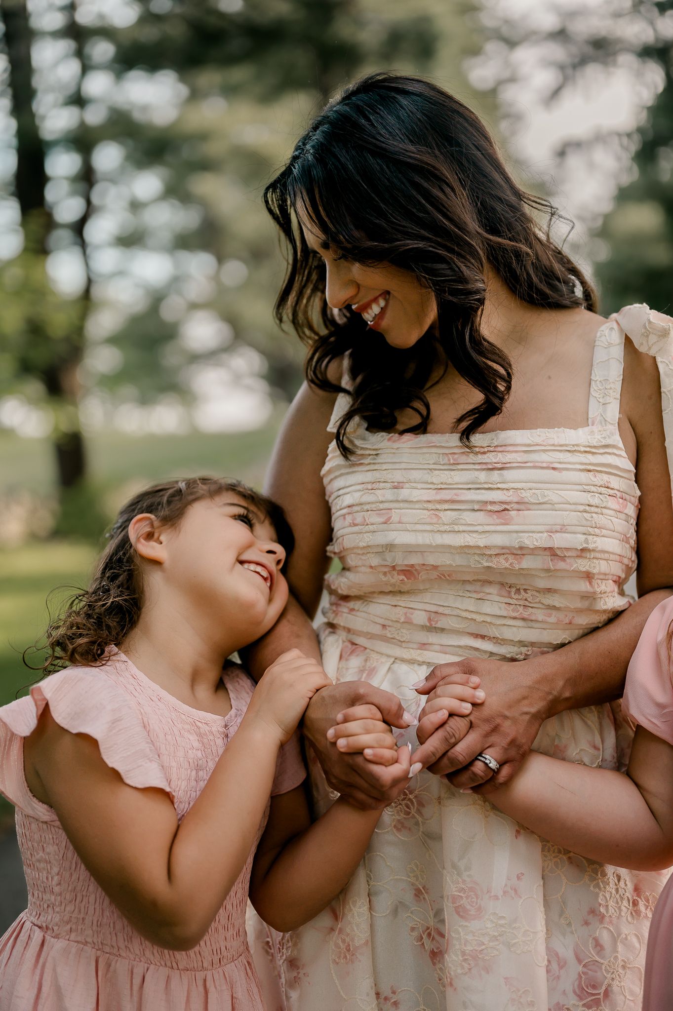 Mother in floral dress smiling warmly at young daughter in pink dress outdoors.
