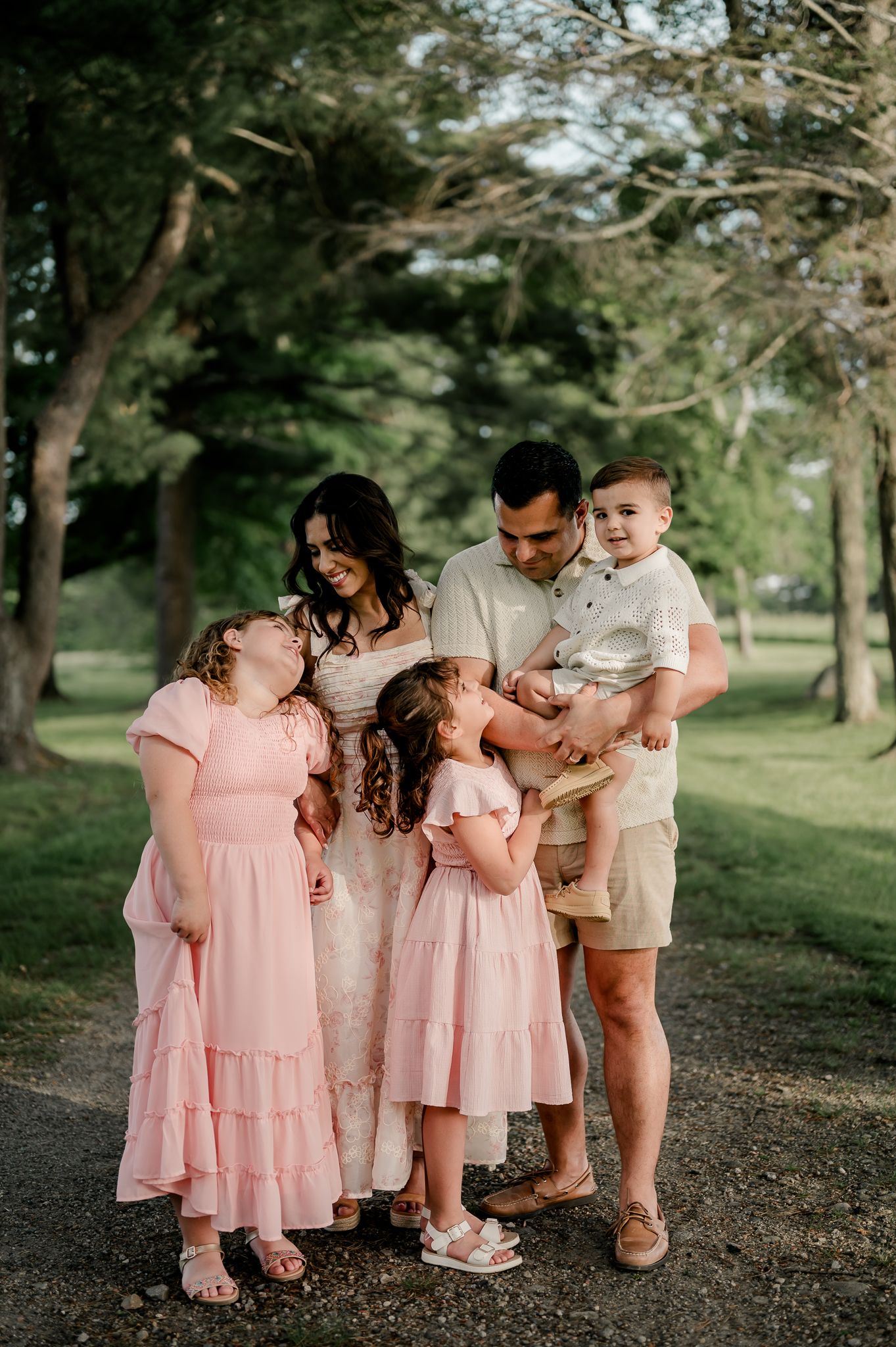 A family of five shares a warm moment together on a tree-lined path outdoors.