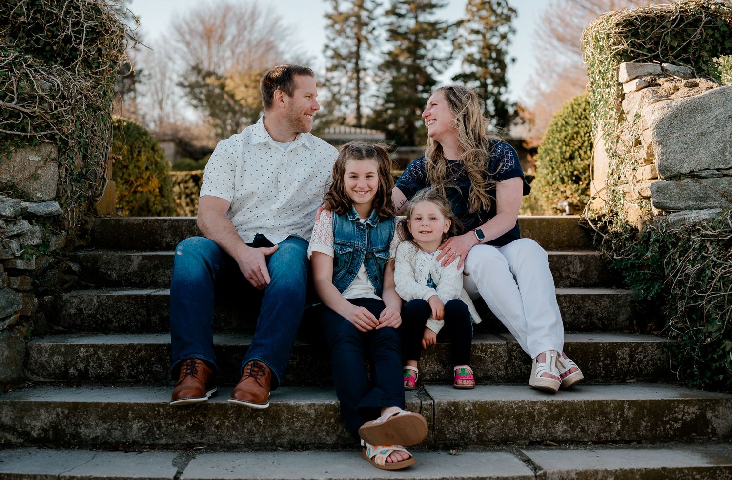 Joyful family of four sitting together on stone steps surrounded by lush greenery outdoors.