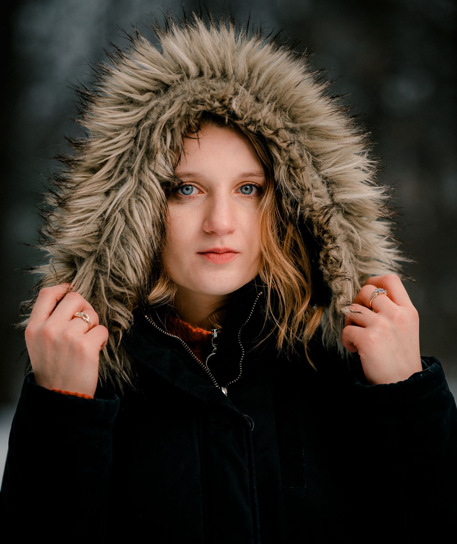Young woman with blue eyes wearing a fur-trimmed hooded black winter coat in snowy setting.
