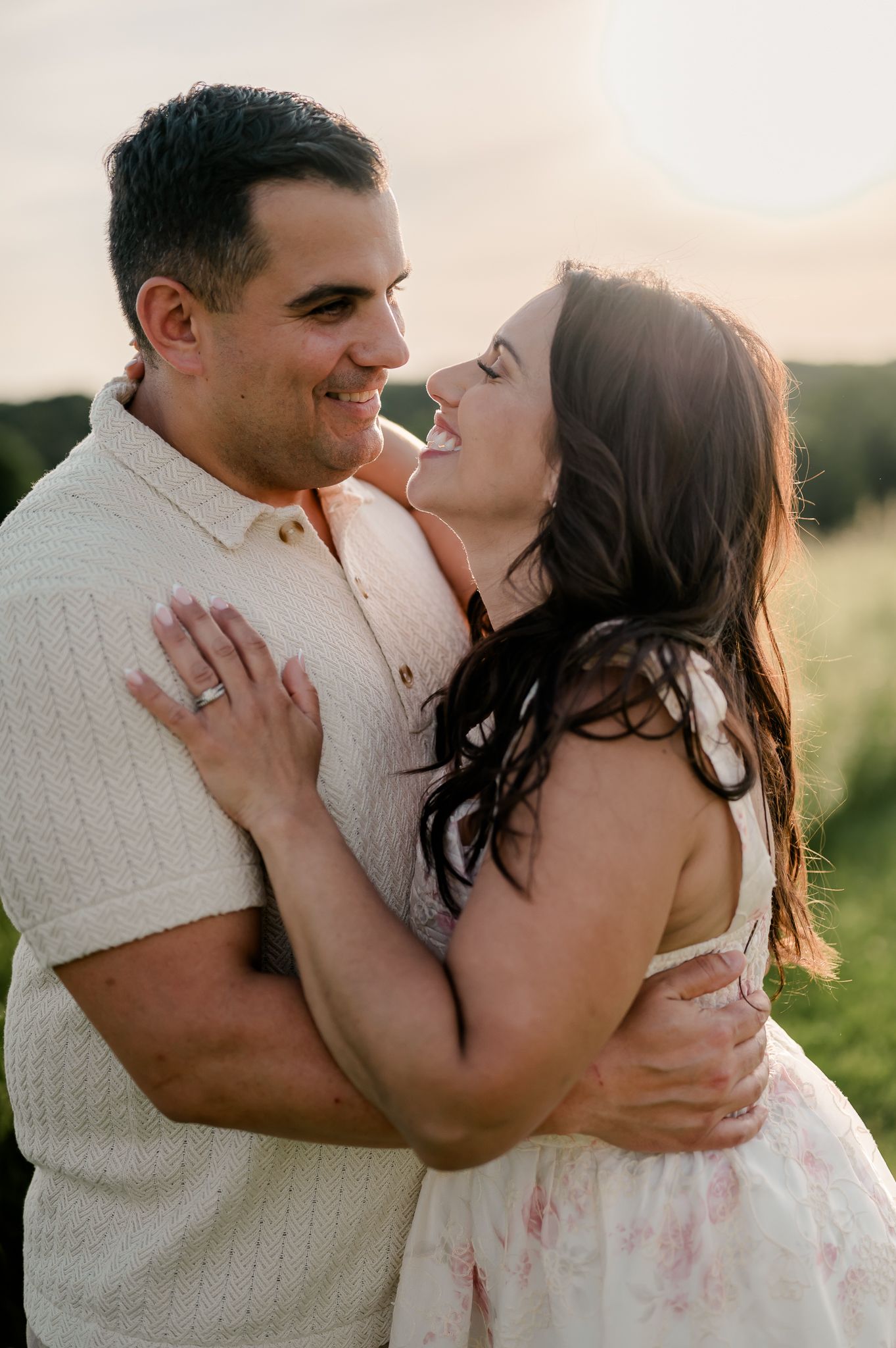 A happy couple embraces and laughs together in a sun-drenched outdoor engagement photo session.
