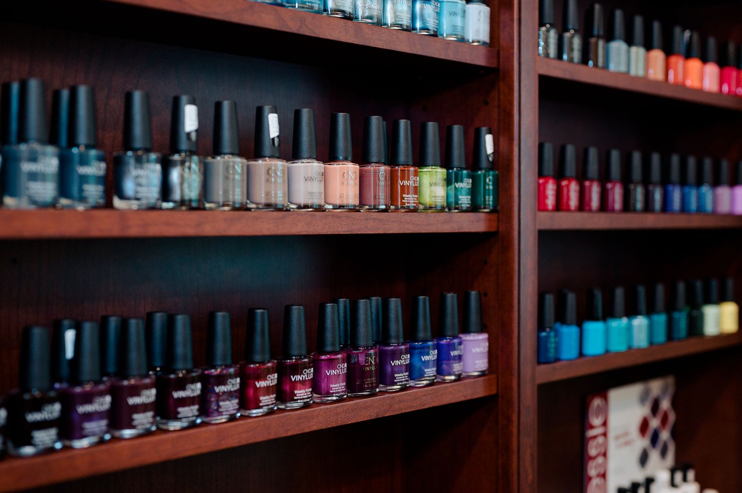 Colorful nail polish bottles displayed on wooden shelves in a nail salon, showcasing a wide variety of shades.