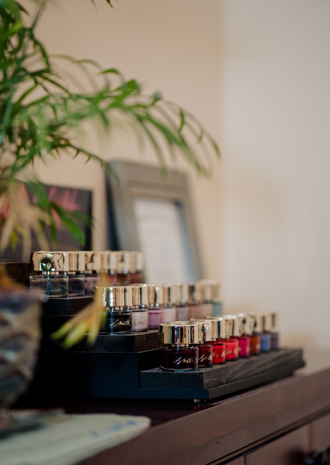 Row of colorful nail polish bottles displayed on a black tiered rack in a nail salon.