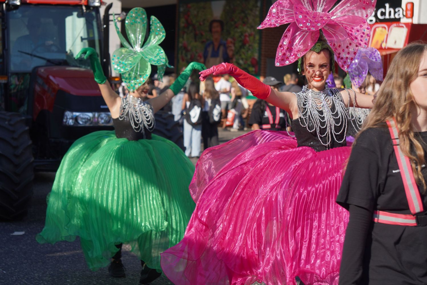 An entertainer at Sydney's Royal Easter Show is performing in a parade. She is wearing a dress with a large pink skirt, fascinator, & gloves