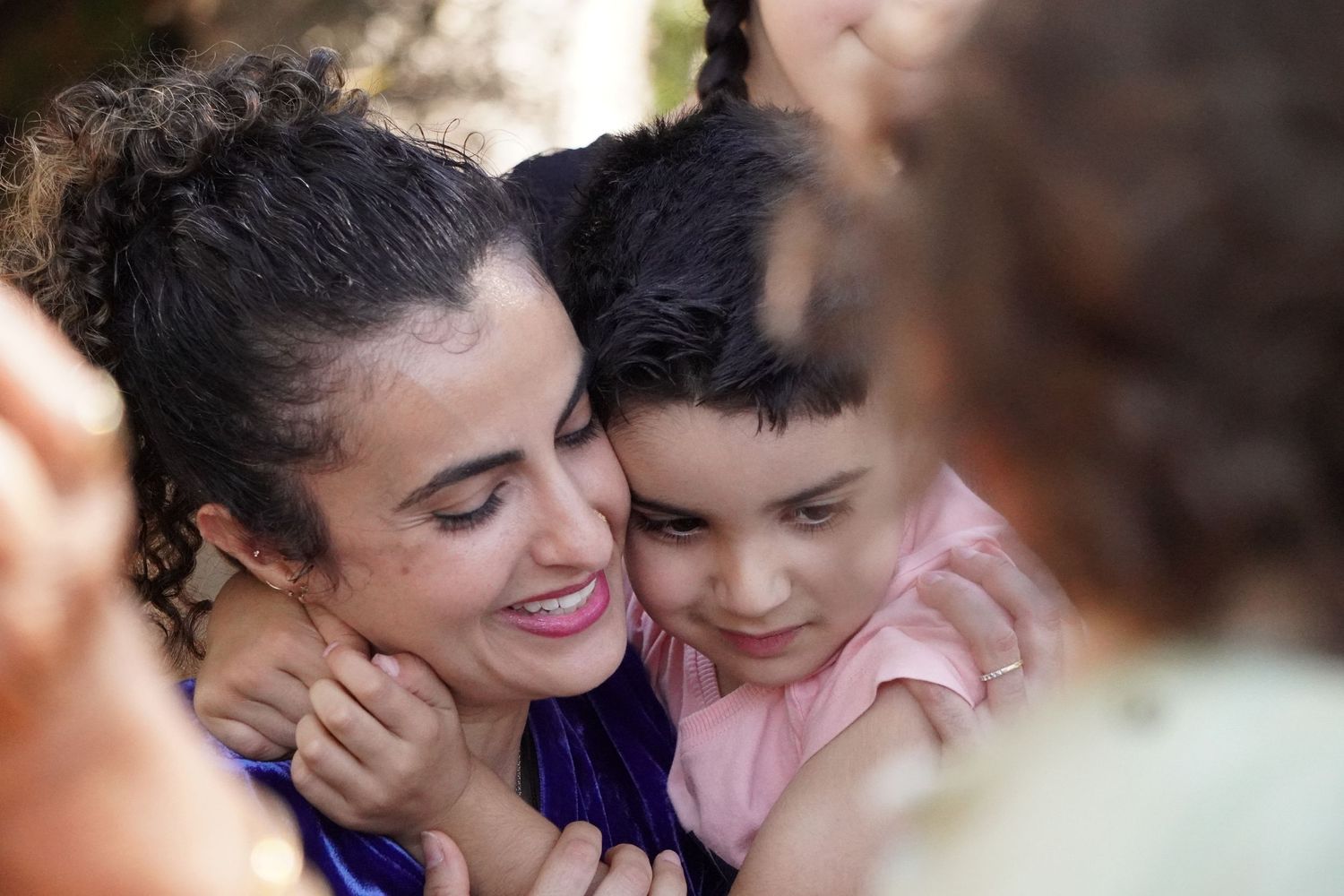 A young boy with black hair closely embraces his mother.