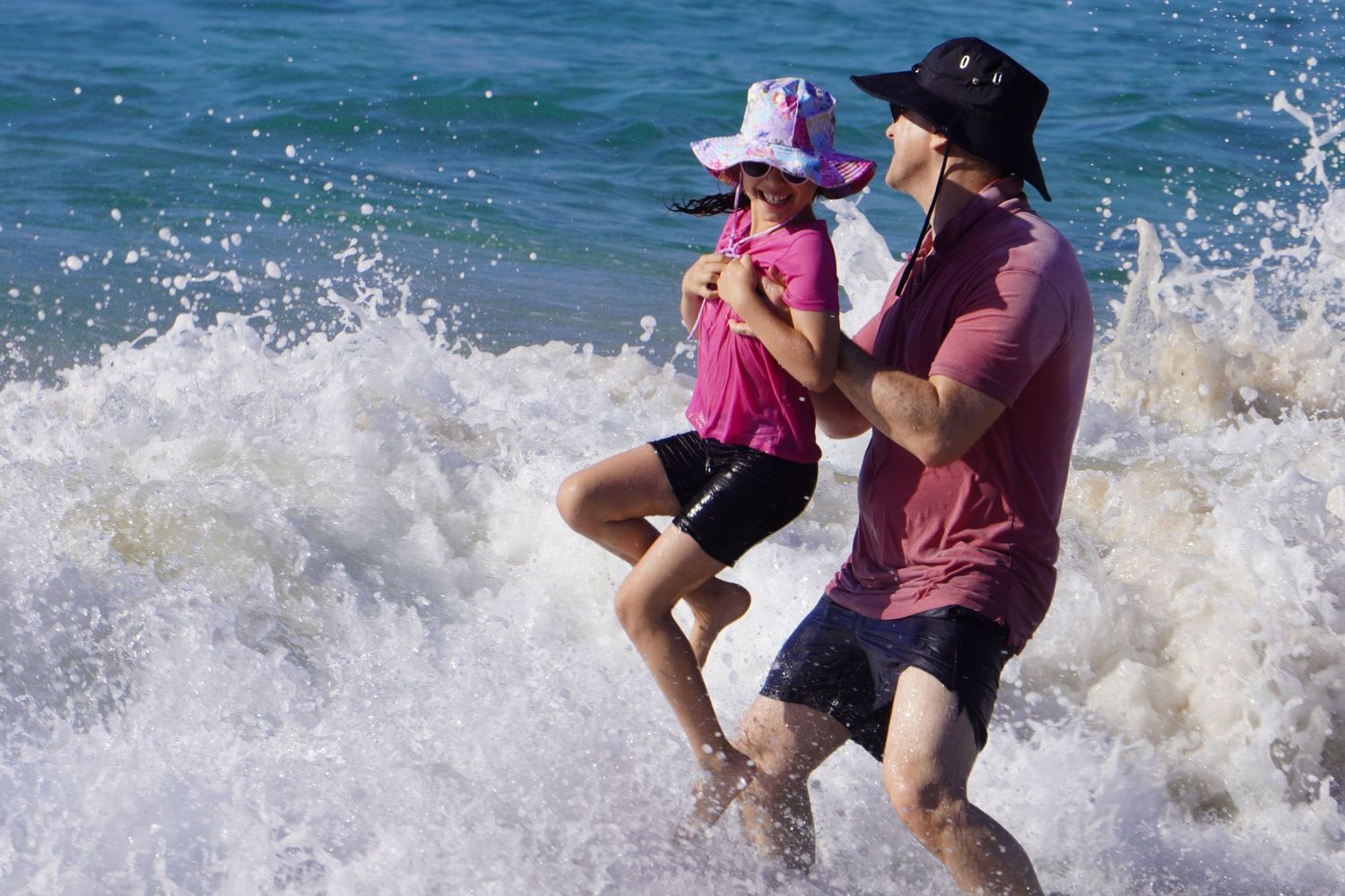 A father and daughter playing in the waves at the beach.