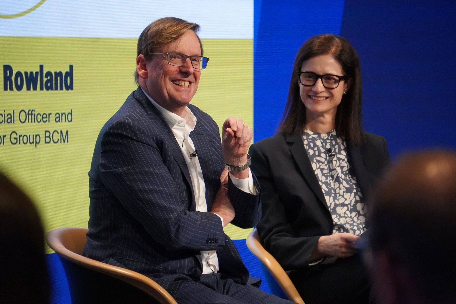 Documentary photo of a corporate interview panel with a man and woman speaking on stage at a Sydney business event.