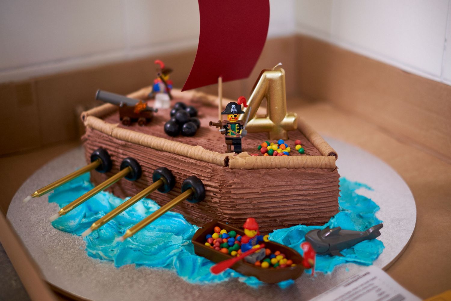 A fourth birthday cake in the shape of a pirate ship complete with lego pirate figurines and lolly treasure.