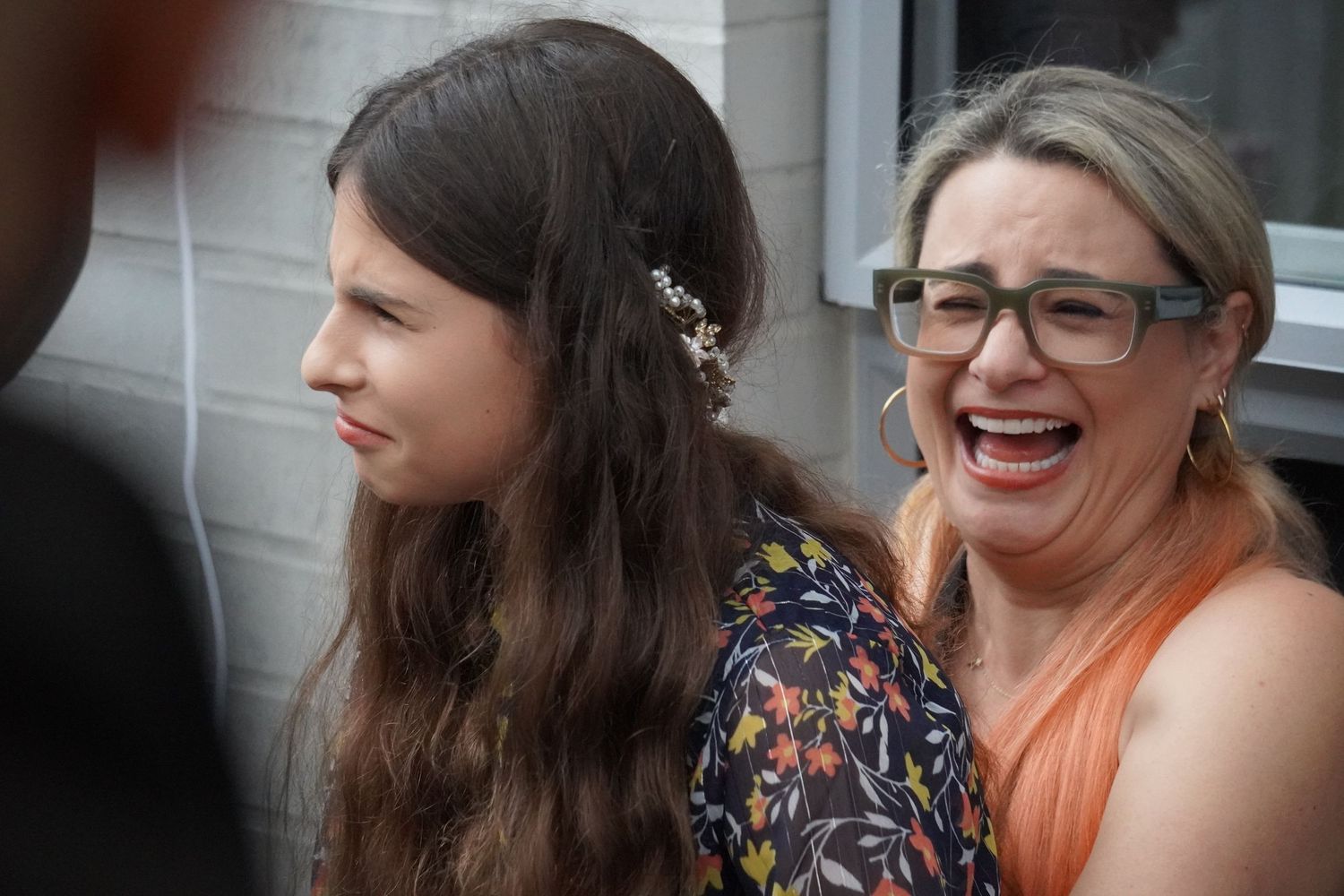 A mother and daughter at an event listening to a speech. The mother laughs and the daughter makes a confused face.