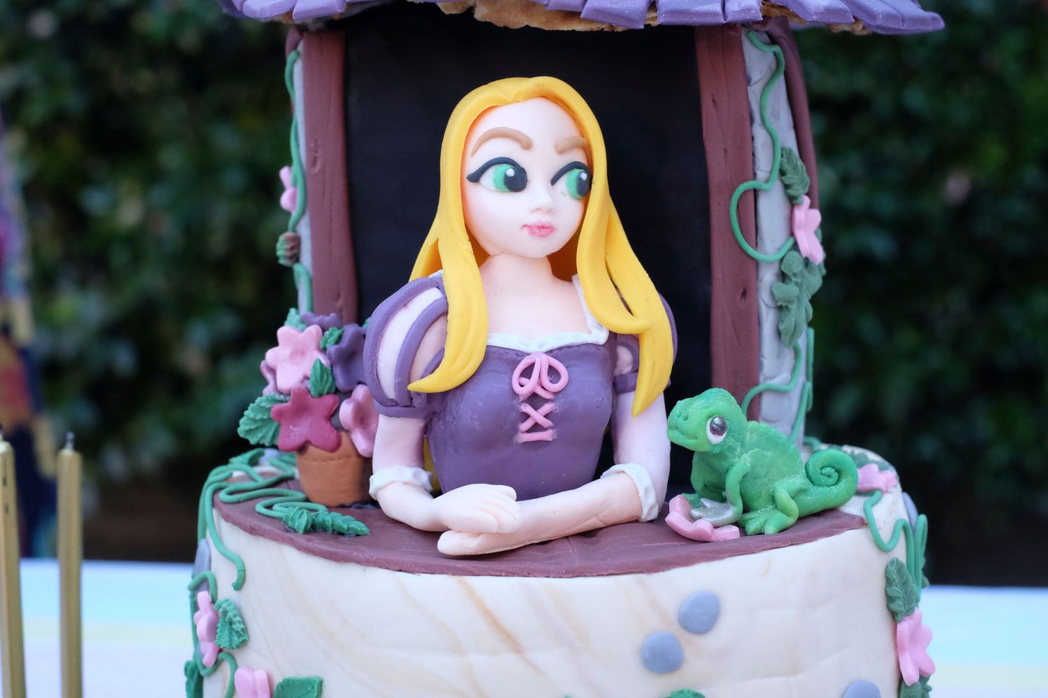 A close frame photo of a birthday cake that looks like Rapunzel's tower. The fondant Rapunzel is glancing out of her flower-covered window.