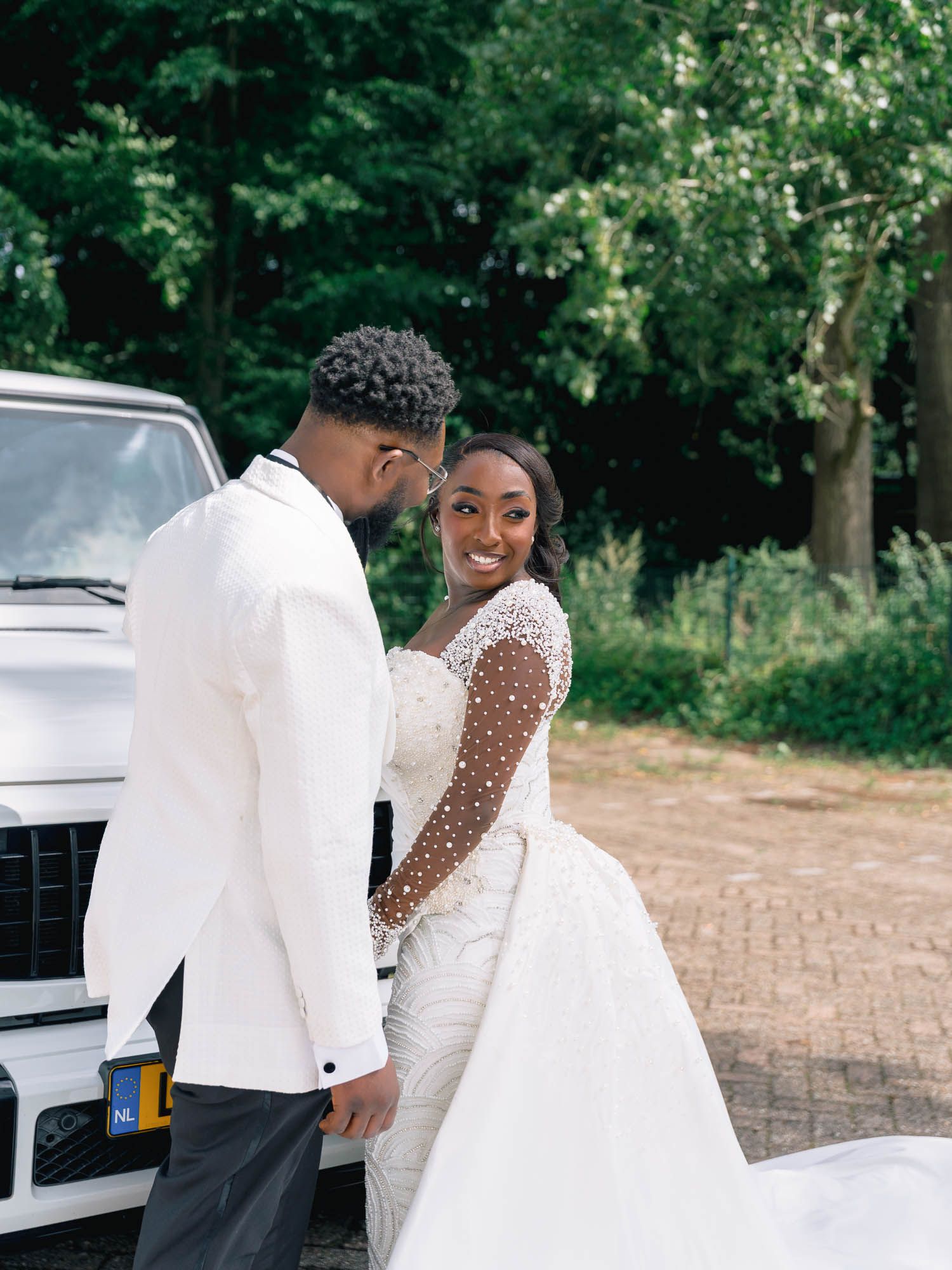 Bride and groom embracing outdoors next to a luxury white Mercedes G-Wagon wedding car