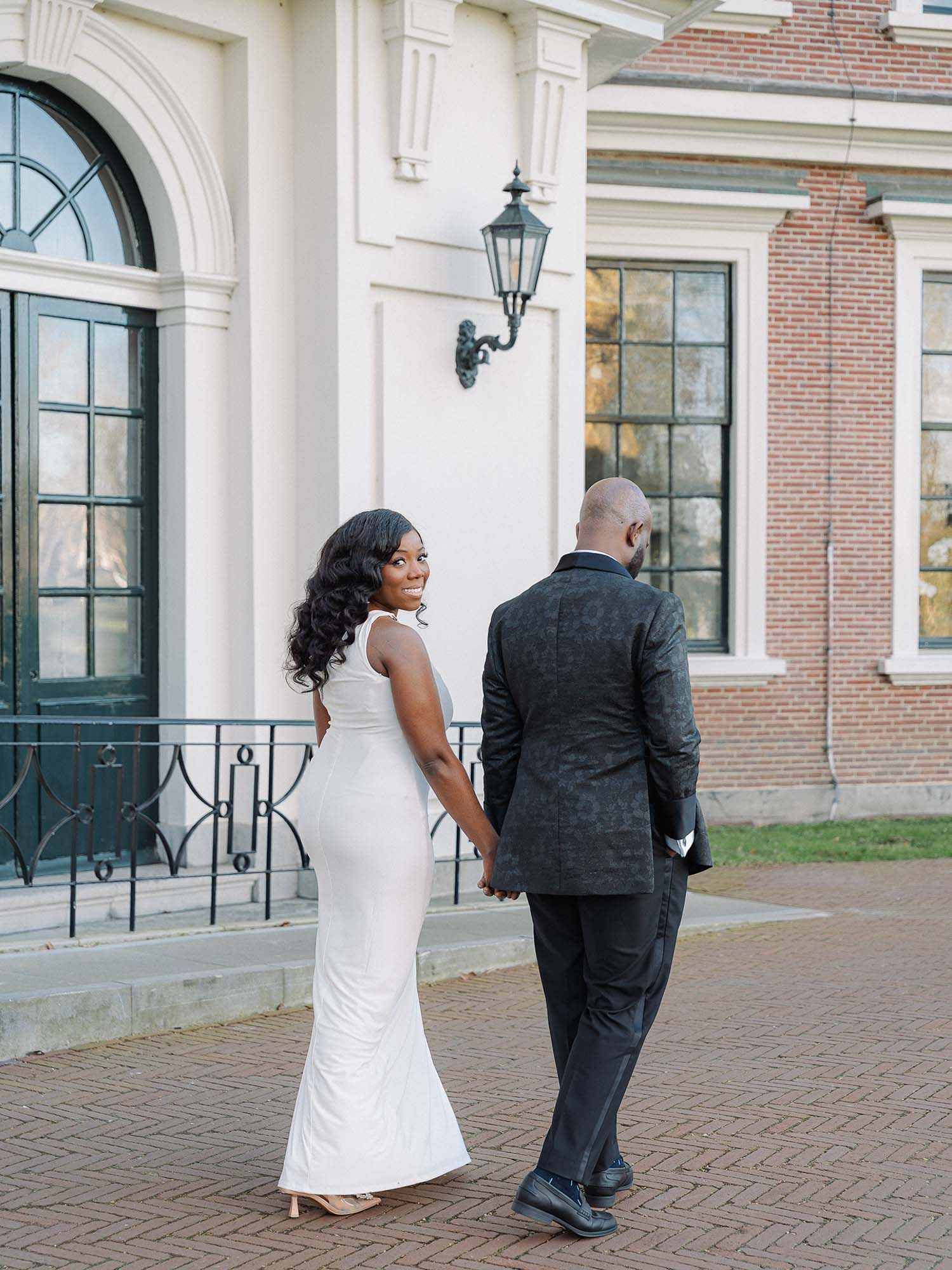 Yaw and Nic walking hand-in-hand outside a classic estate during their pre-wedding photoshoot.