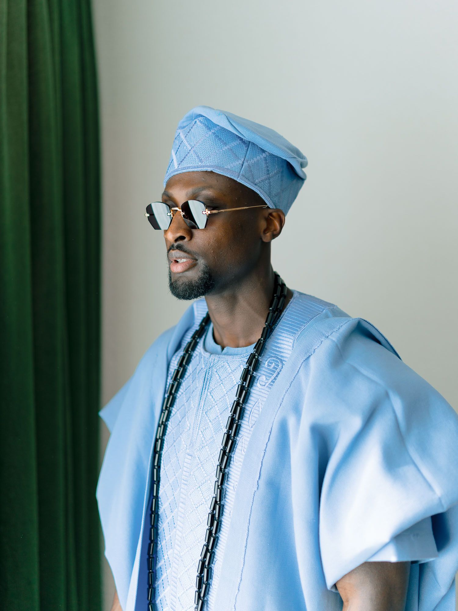 Portrait of a man wearing a traditional light blue embroidered Agbada and matching cap