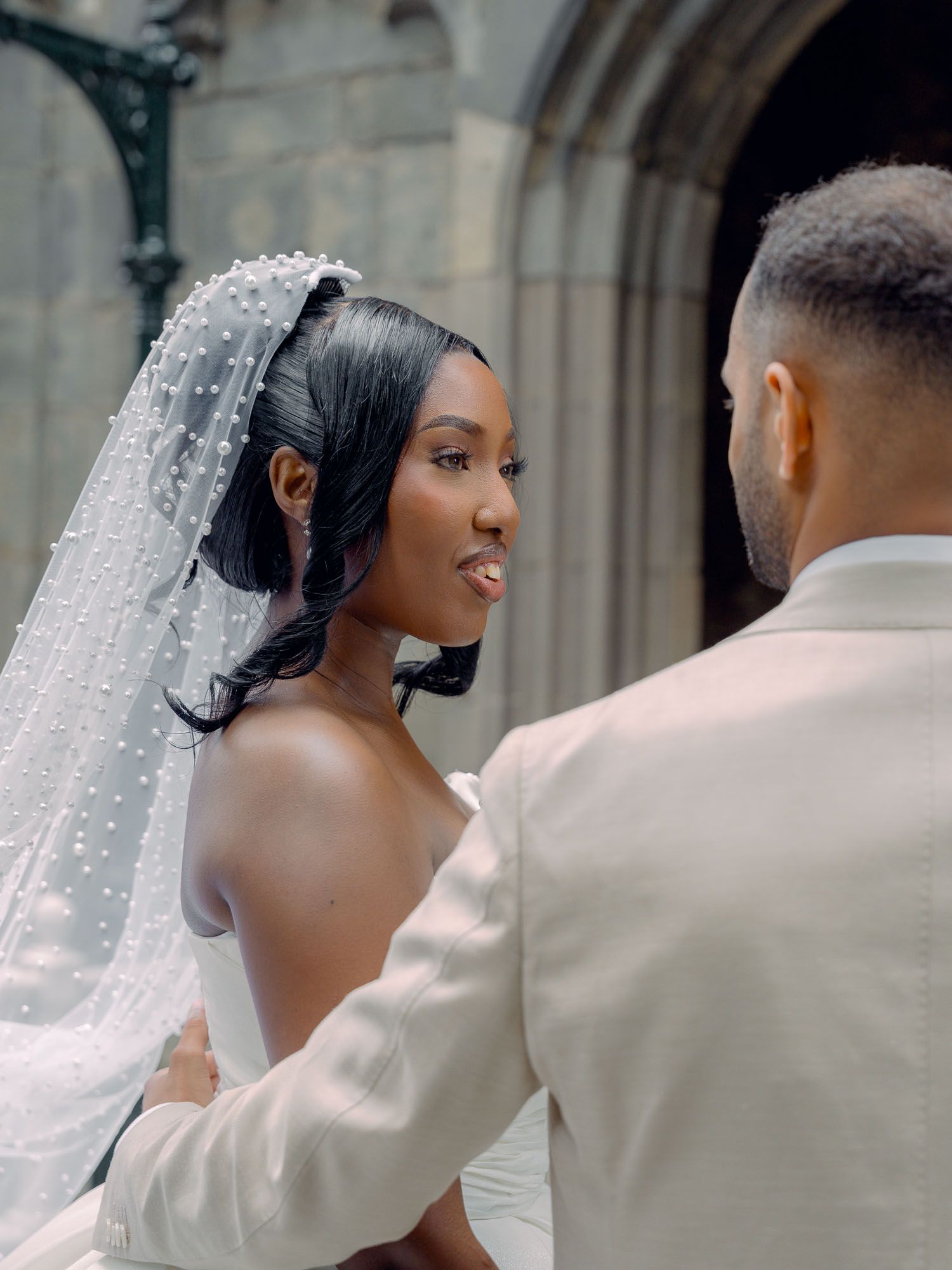 Close-up romantic portrait of a bride with a lace wedding veil smiling lovingly at her groom