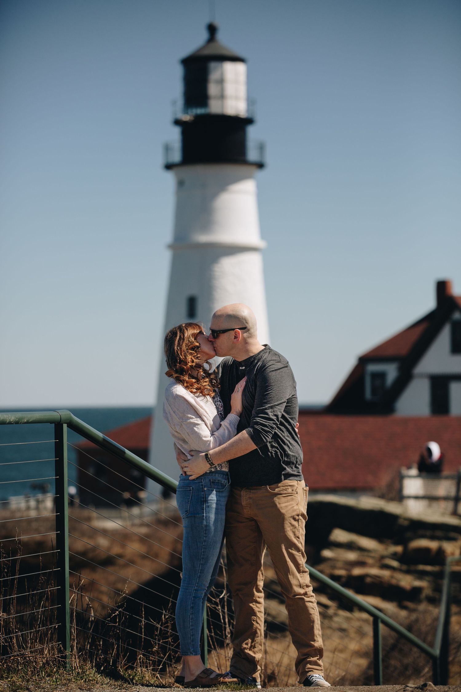 A couple shares an intimate moment in front of a classic New England lighthouse.