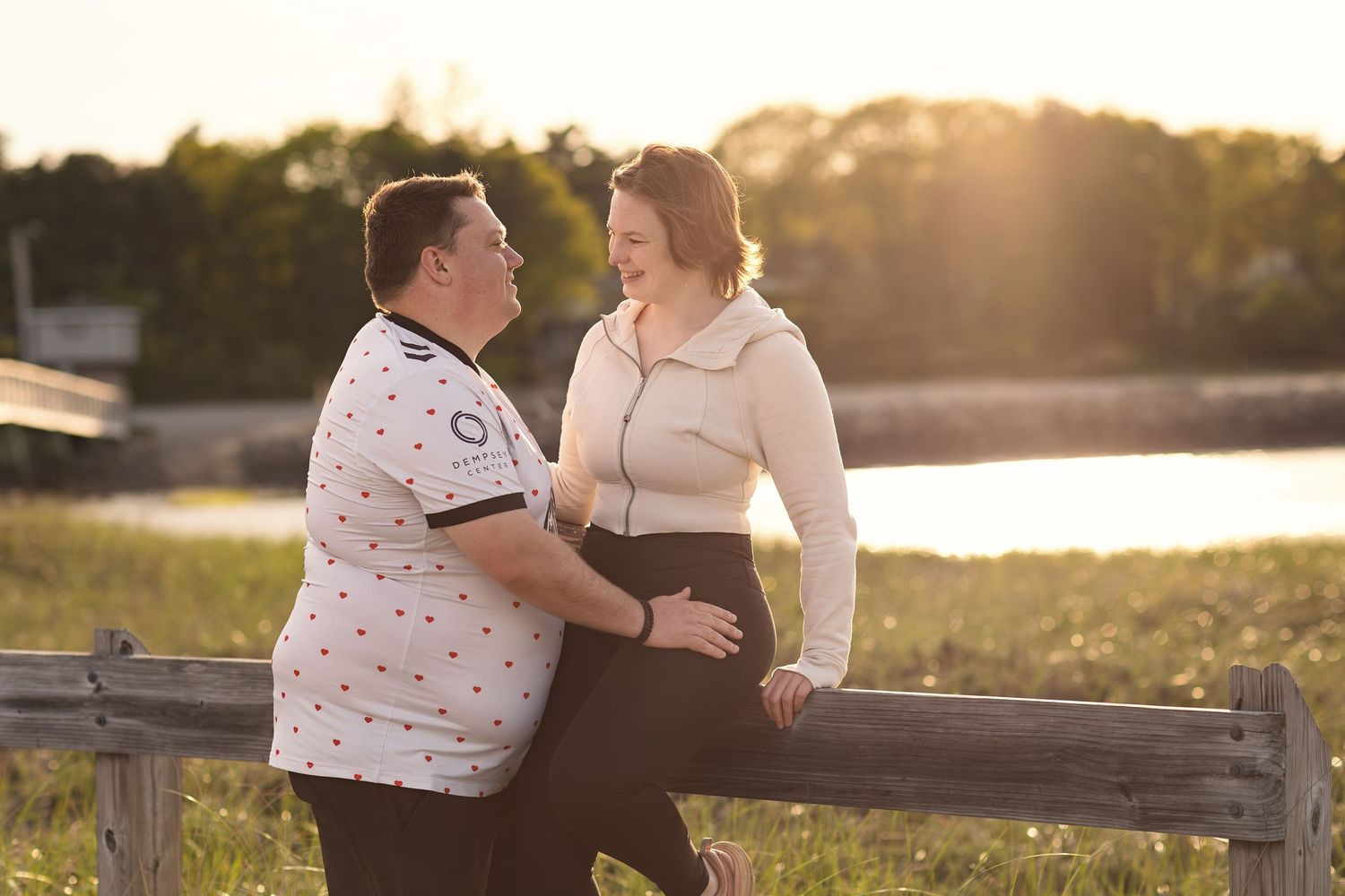 Couple sitting on wooden fence during golden hour sunset.