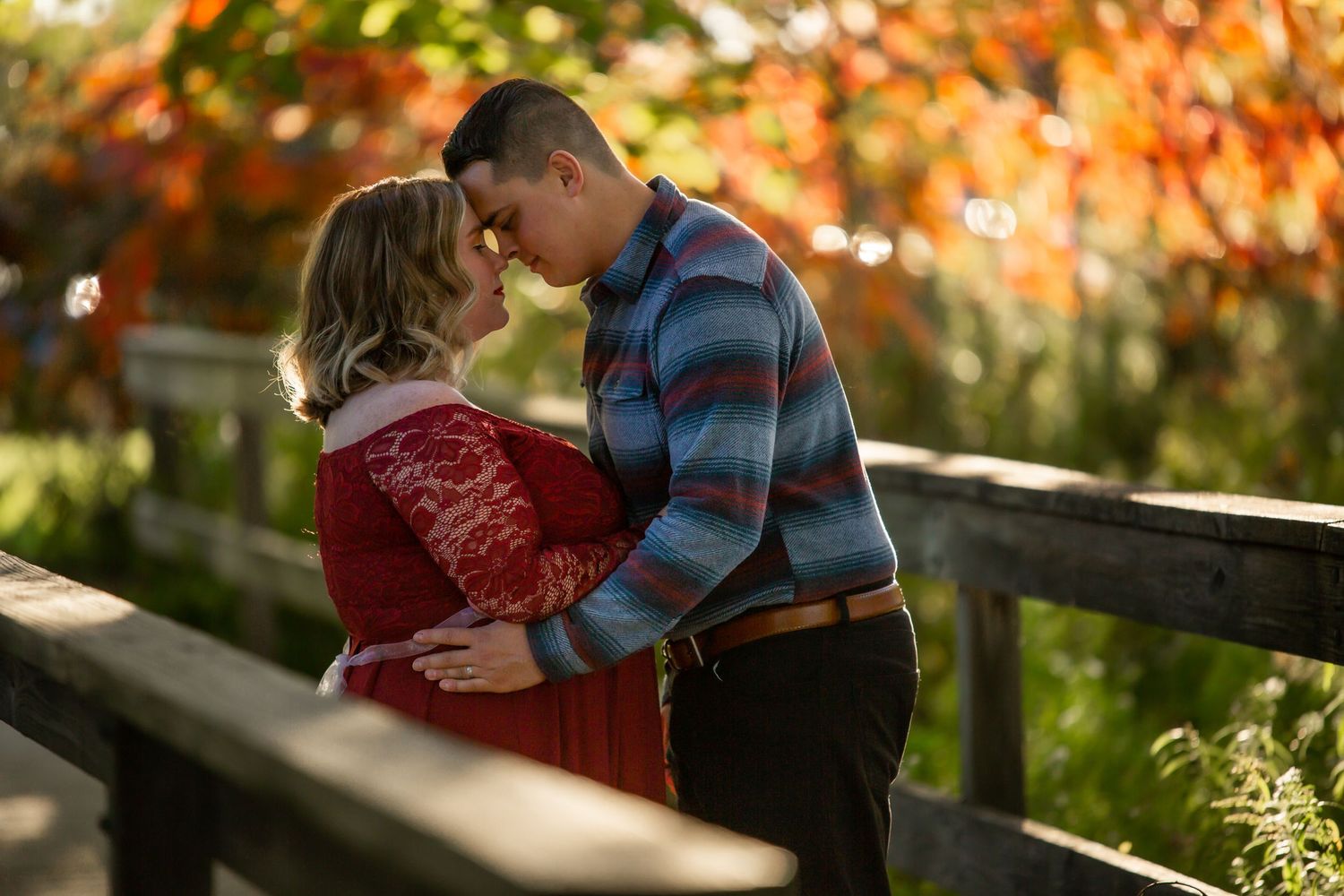 A romantic autumn moment shared between a couple on a wooden bridge surrounded by vibrant fall foliage.
