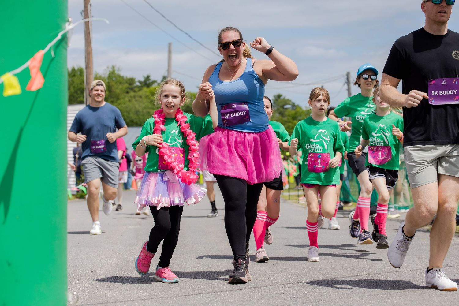 Women and children in pink tutus running together in outdoor charity fun run race on sunny day.