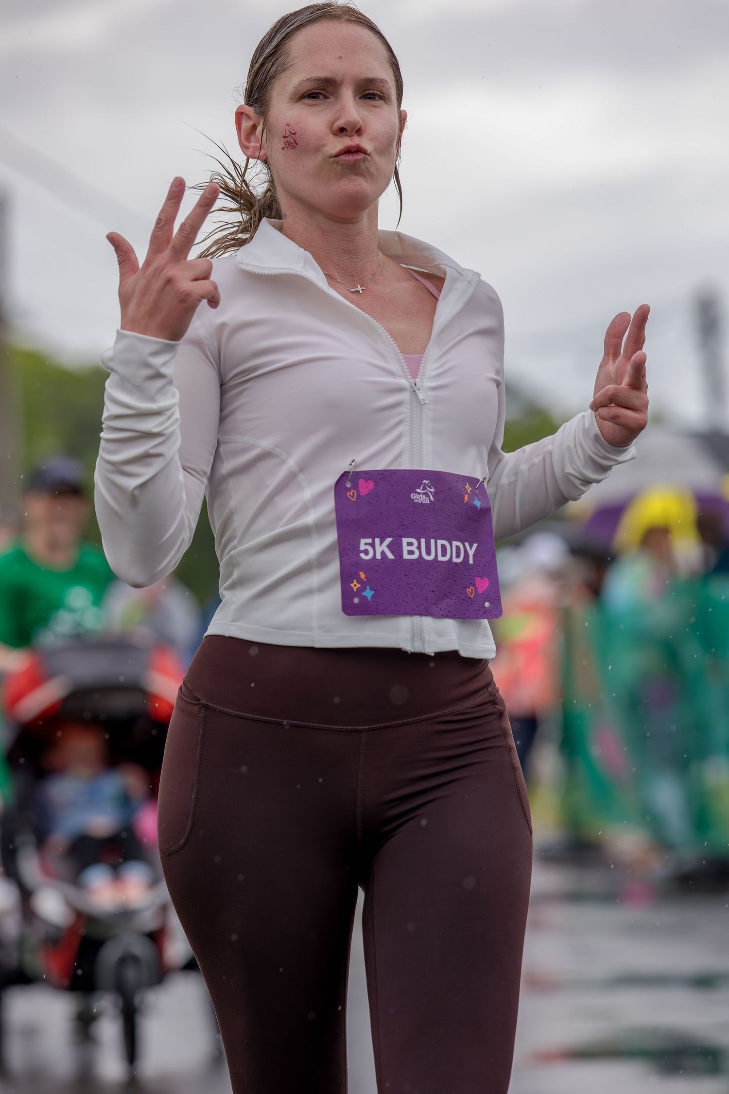 Woman wearing a 5K Buddy race bib gestures with both hands during a rainy outdoor running event.