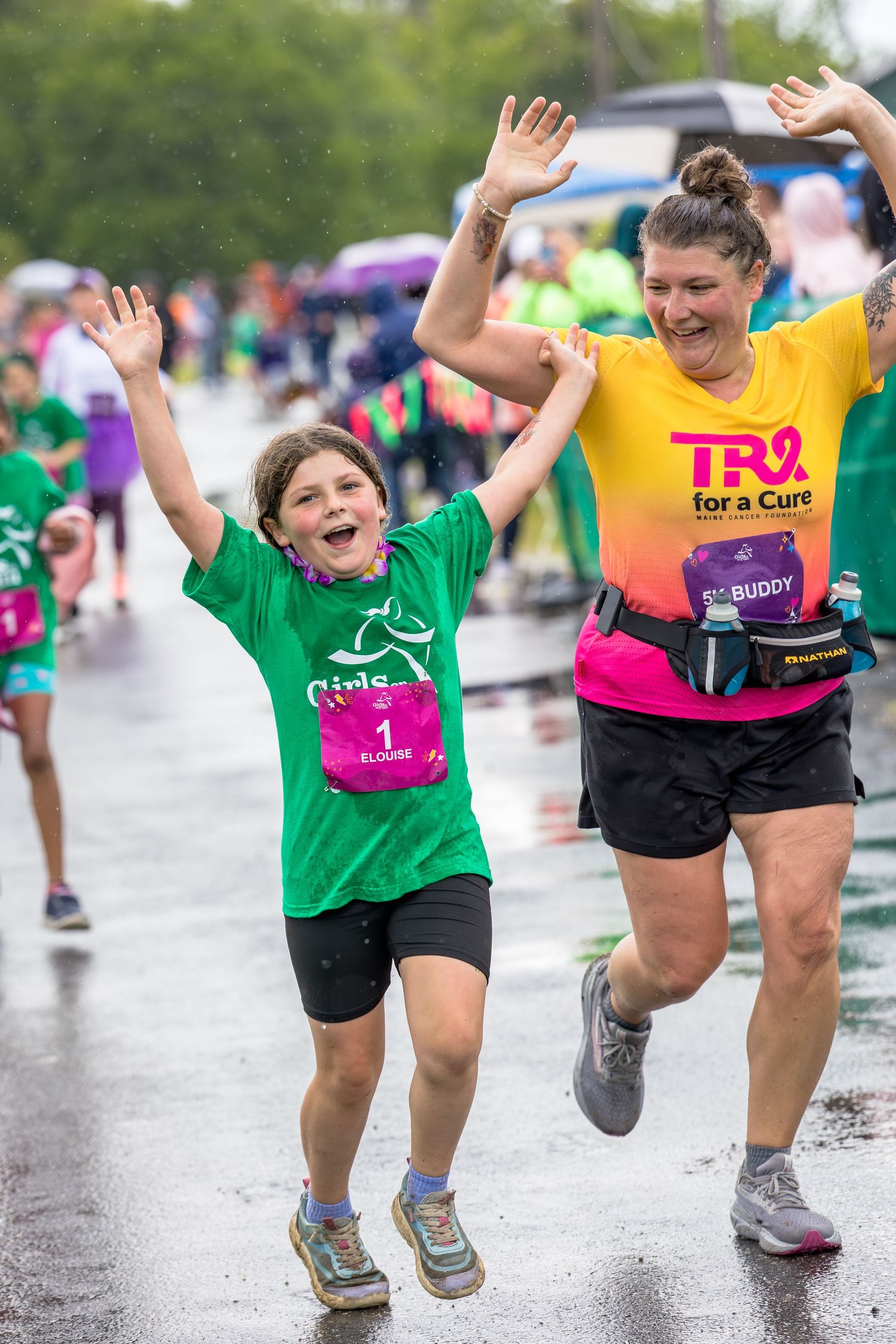 Two joyful runners celebrate in the rain at a charity race, wearing green and yellow Try for a Cure event shirts.