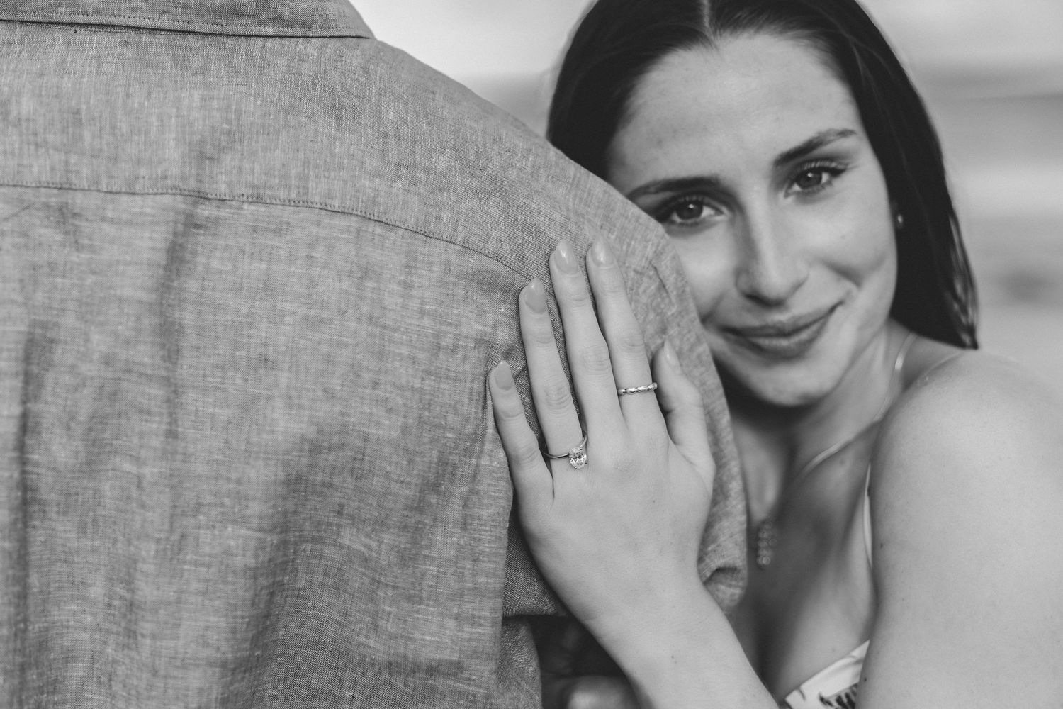 Black and white photo of a smiling bride leaning on groom, showing engagement ring on her hand.