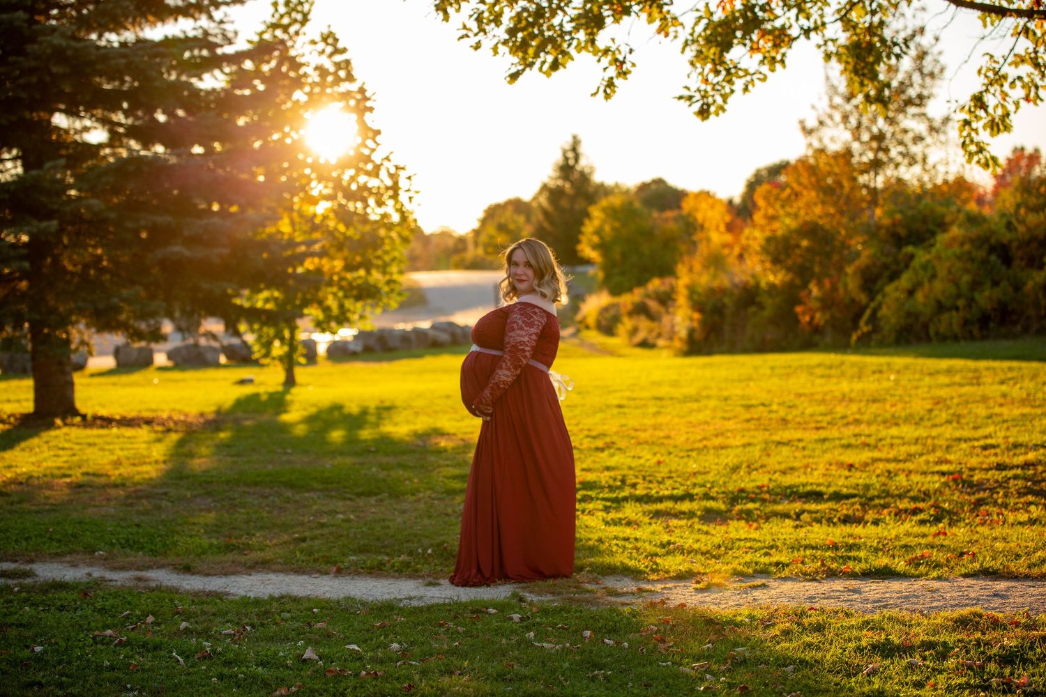 Golden sunset light illuminates a grassy hillside during a romantic outdoor maternity photo session.
