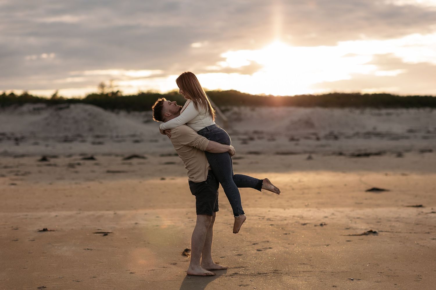 Romantic couple embraces on sandy beach during golden sunset with ocean waves in background.
