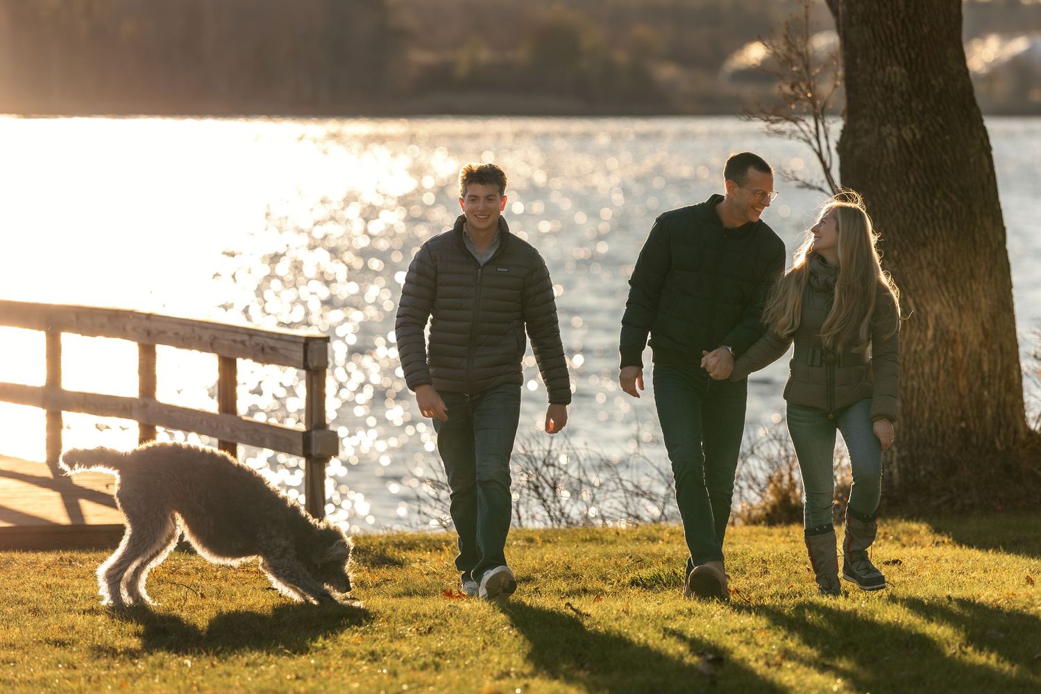 A family of people walking with a dog along a waterfront path during golden sunset hour.