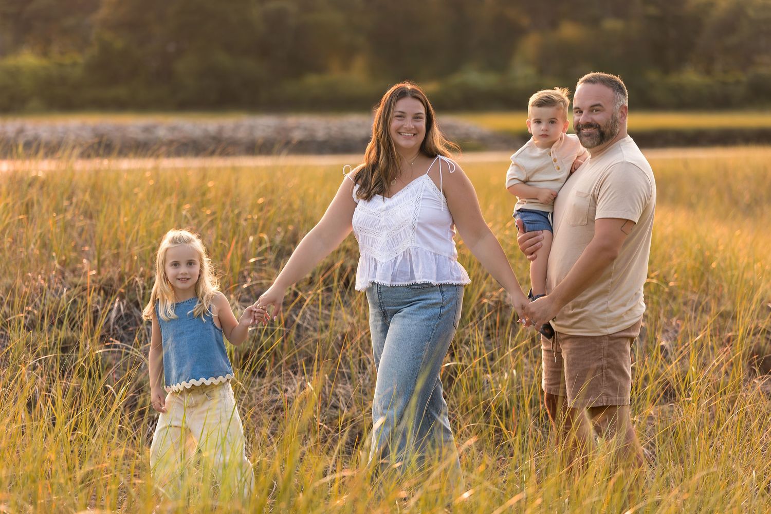 A family stands together in a golden sunlit field of tall grass during sunset.