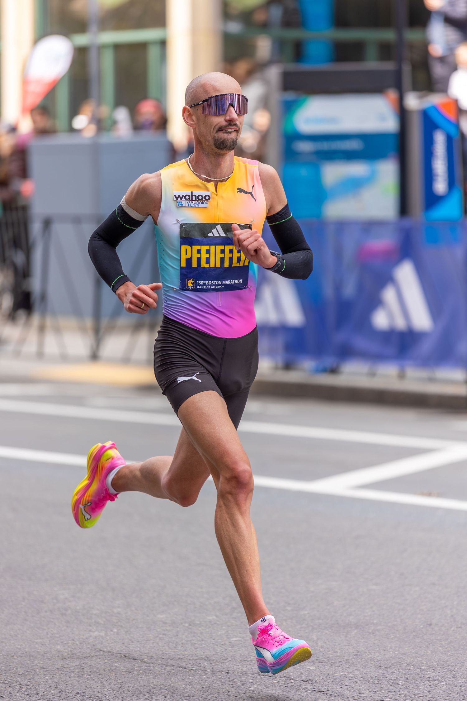 Bald marathon runner Pfeiffer in colorful Puma kit and sunglasses races through city streets during a major marathon event.