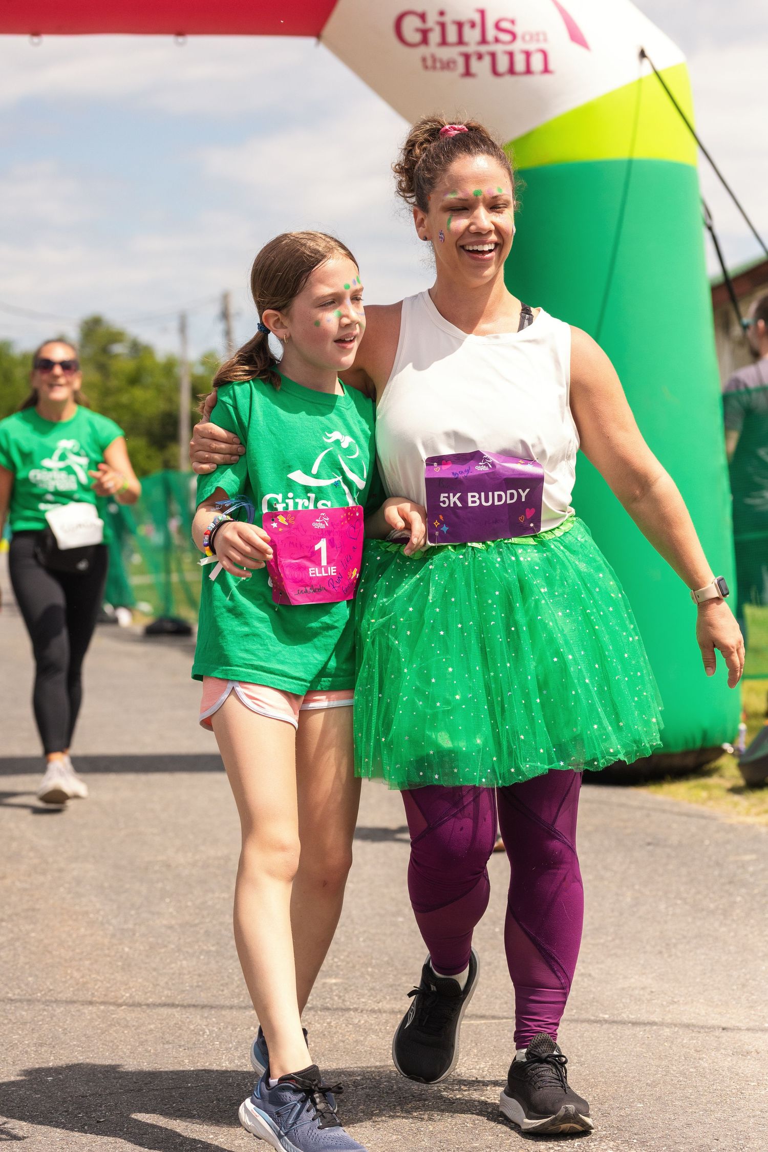 A woman and girl in green outfits walk together at a Girls on the Run 5K race event outdoors.