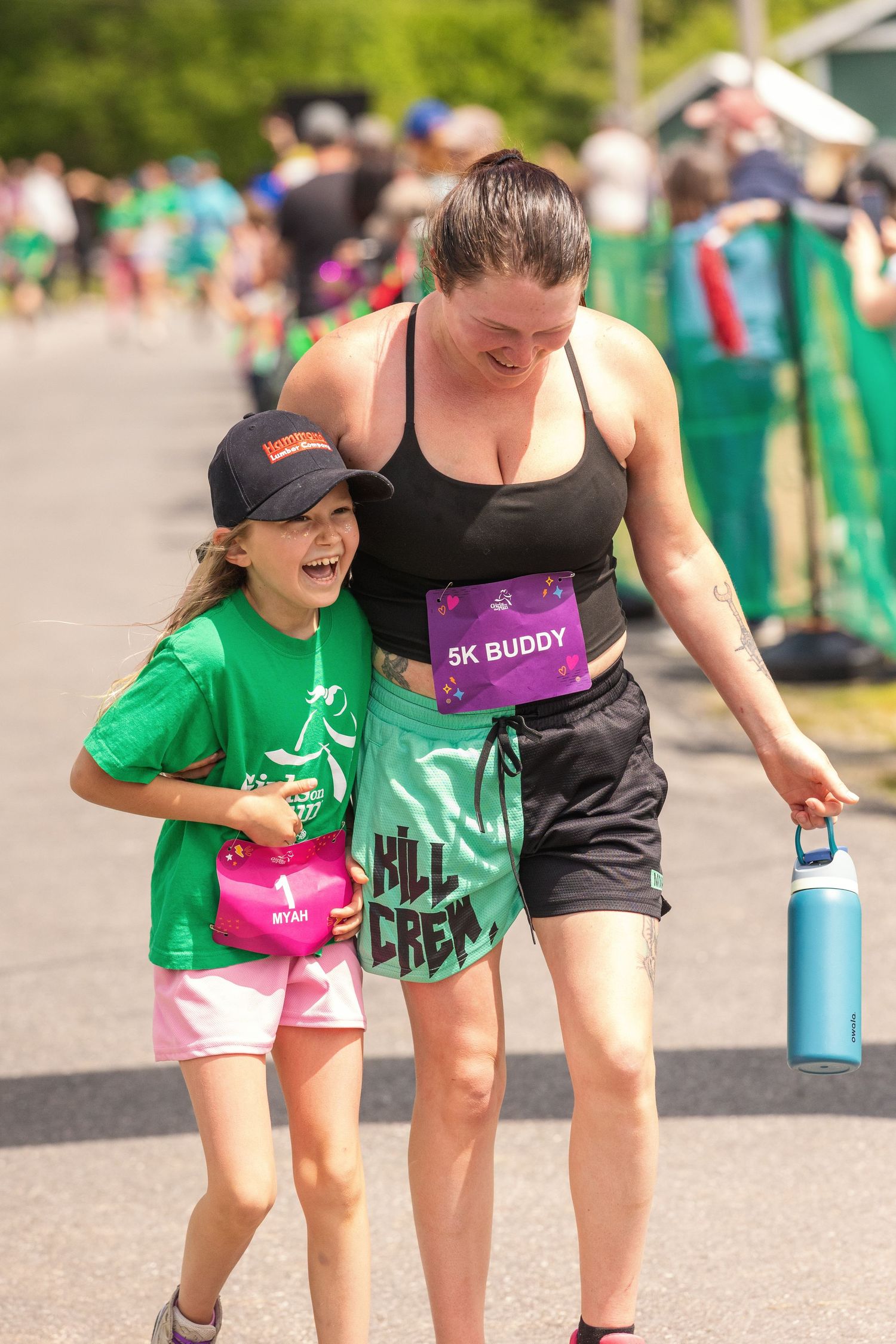 Woman and girl laughing together after completing a 5K buddy run race on a sunny day.