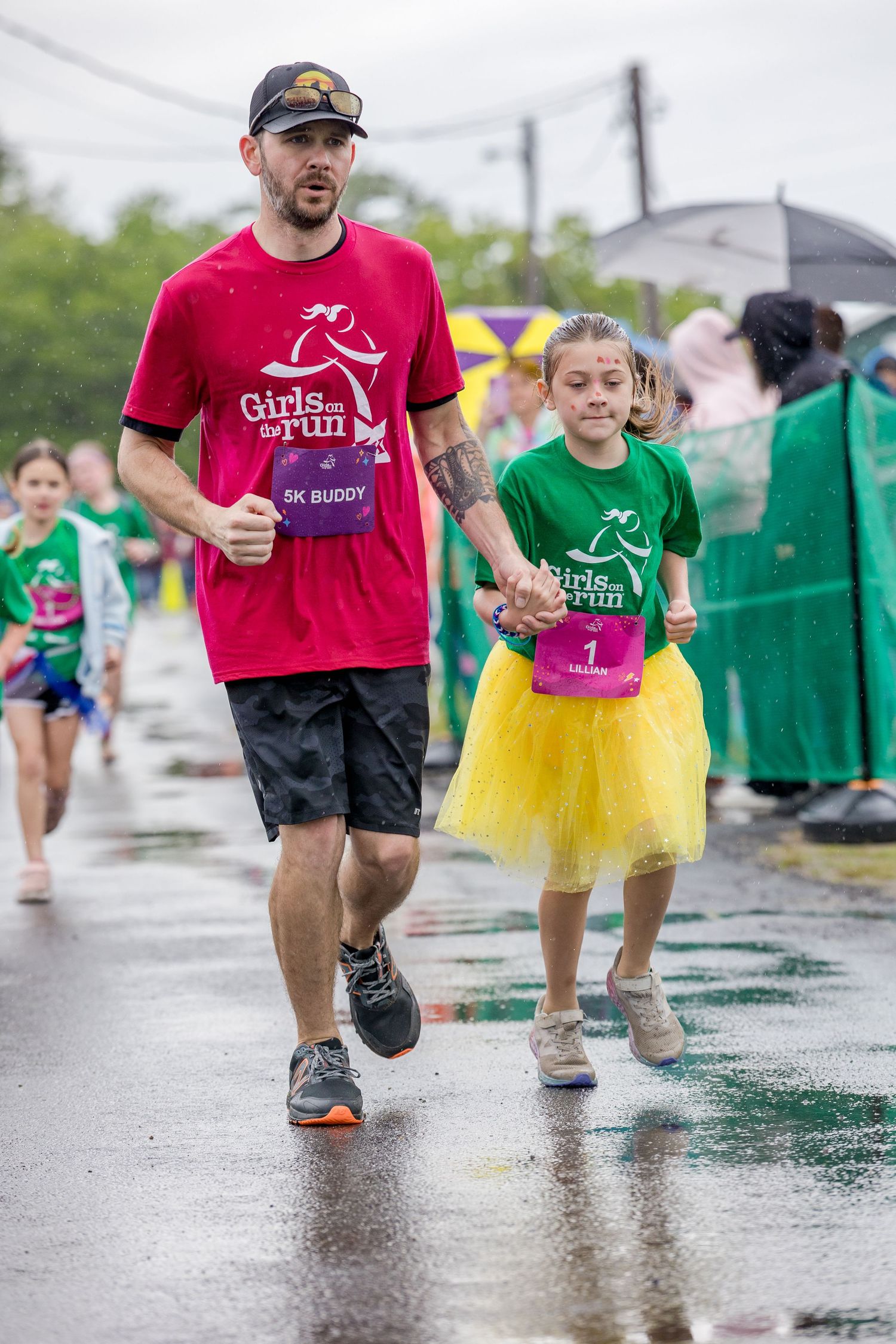 Man and girl in Girls on the Run shirts holding hands during a rainy 5K race.