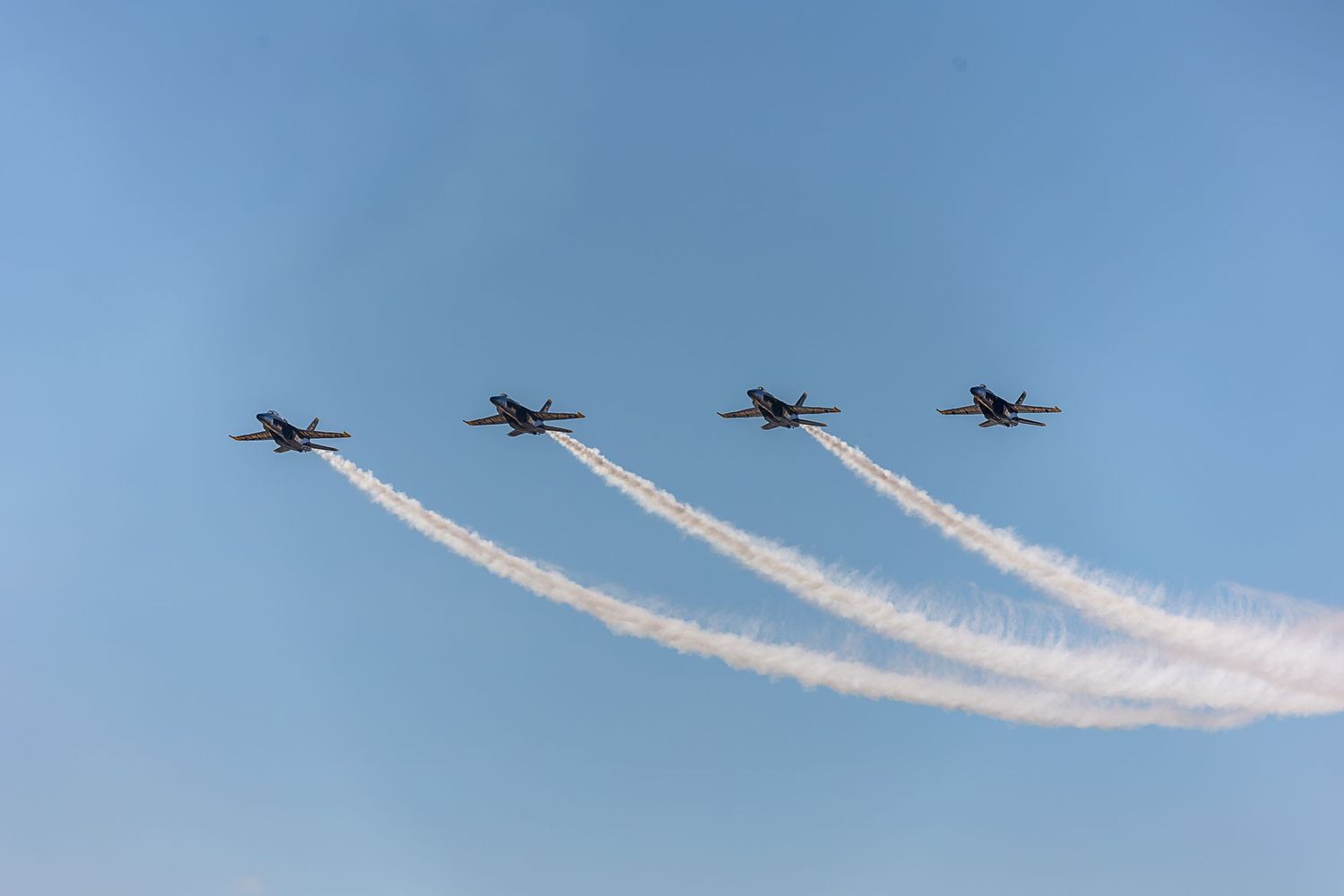 Four airplanes flying in formation against a blue sky leaving white vapor trails behind them.