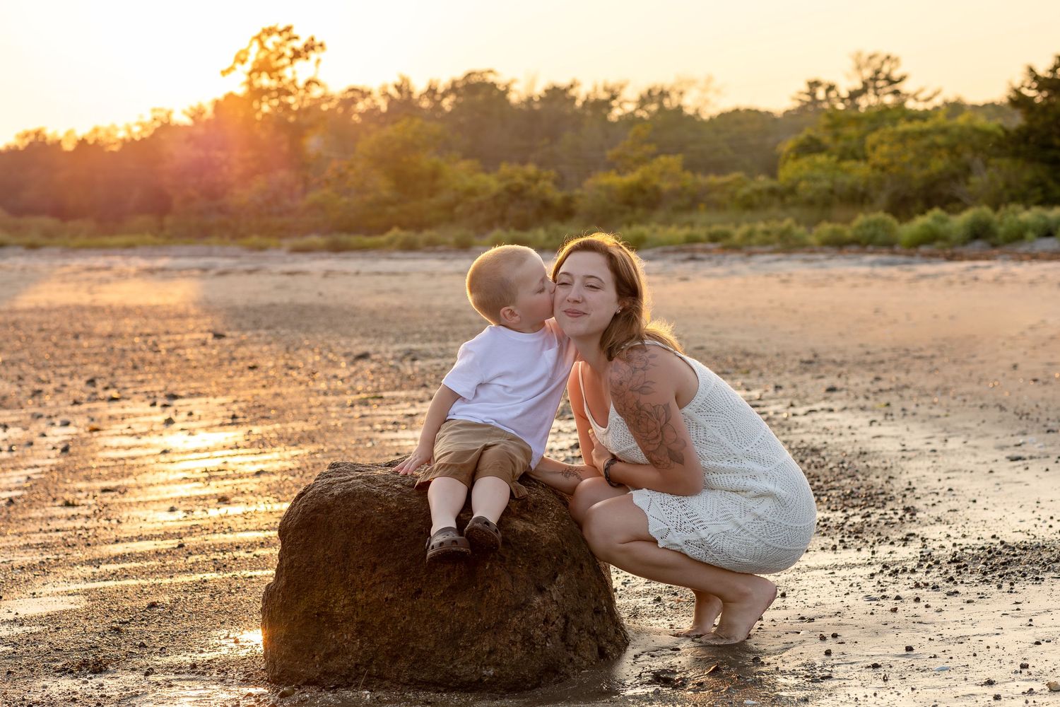 Sunset beach portrait with a large rock and silhouetted trees in the background.