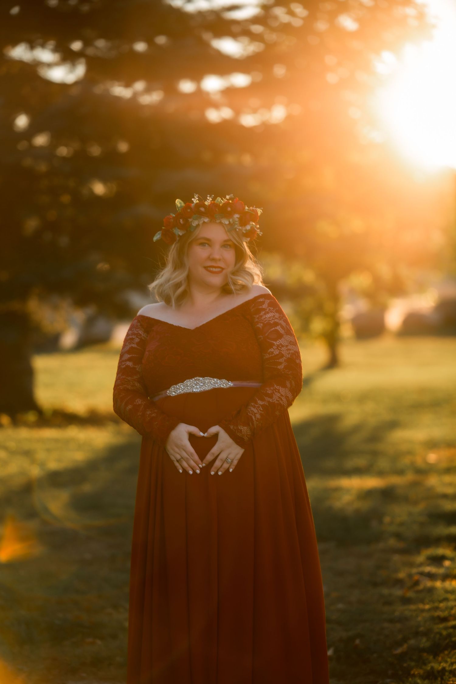 A person in a red dress poses in a golden sunset-lit field making a heart shape with their hands.